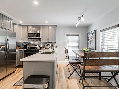Modern kitchen with gray cabinets, stainless steel appliances, and a dining table.
