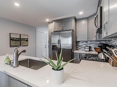 Modern kitchen with stainless steel appliances, gray cabinets, white countertops, and a sink.