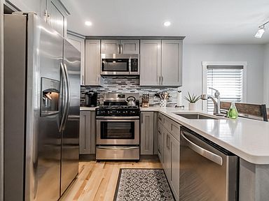 Modern kitchen with stainless steel appliances, gray cabinets, and light wood flooring.