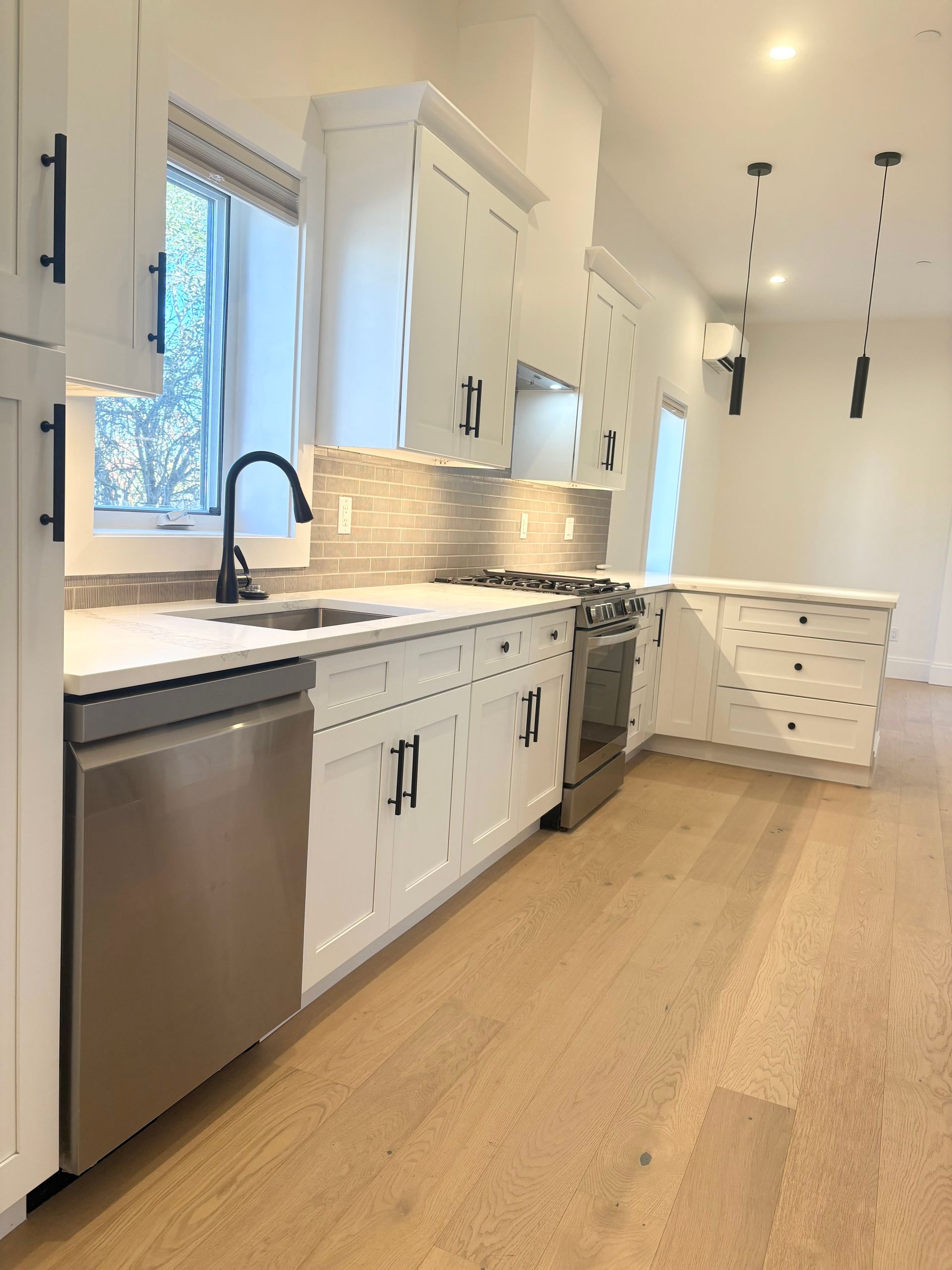 White kitchen with stainless steel appliances, light wood floors, and black hardware.