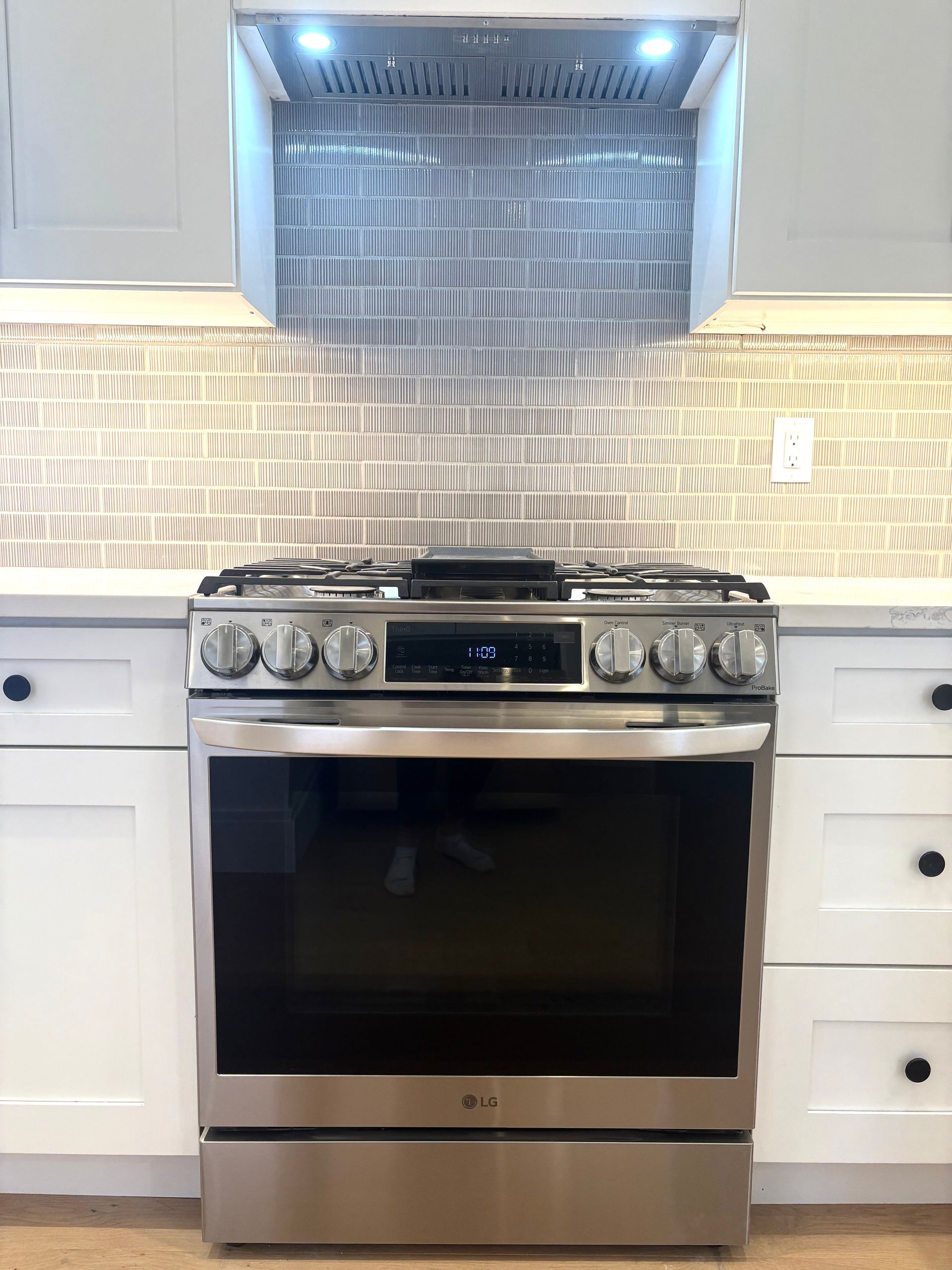 Stainless steel oven and range hood in a kitchen with white cabinets and mosaic tile backsplash.