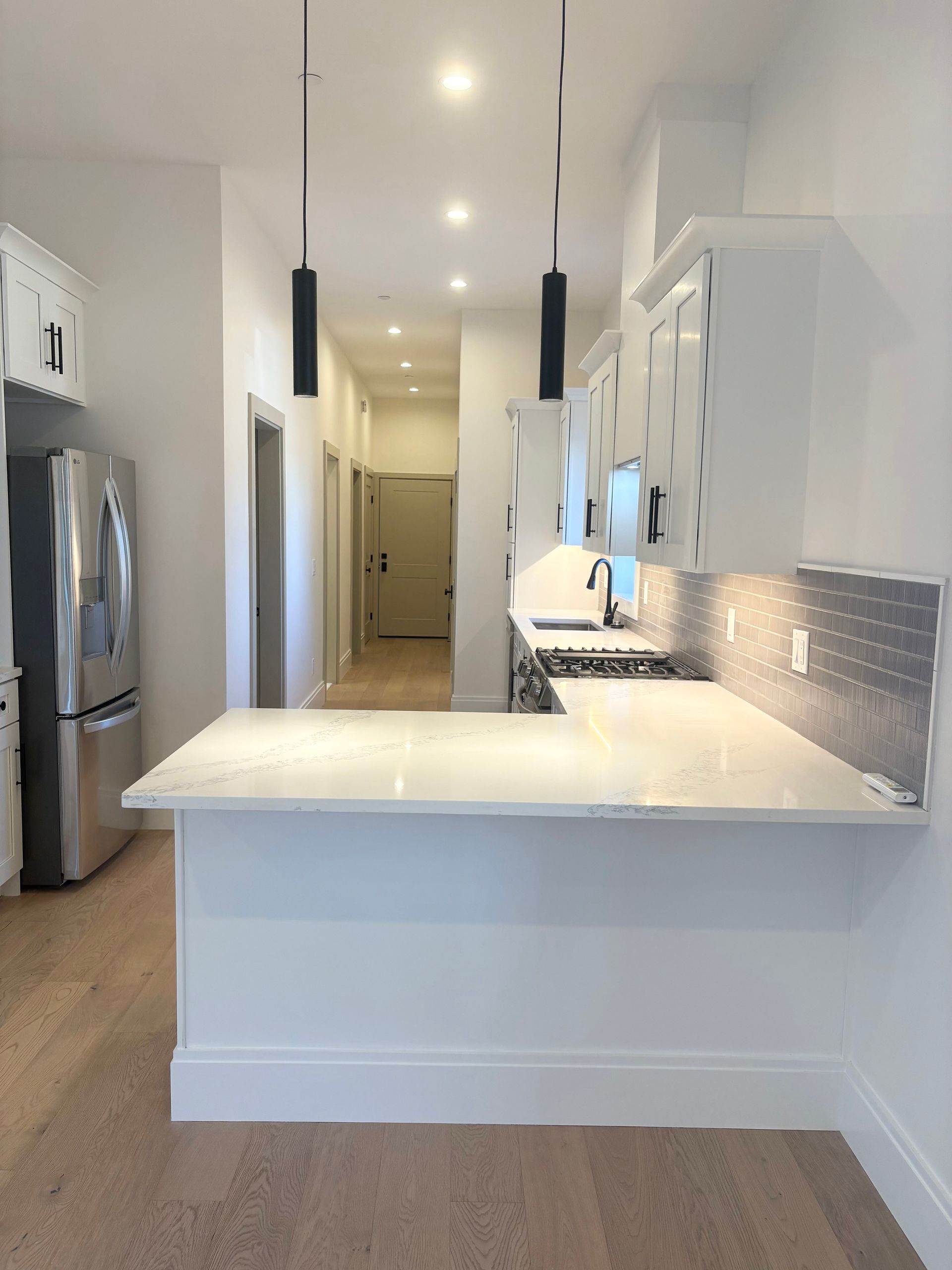White kitchen with peninsula, stainless steel appliances, and hallway.