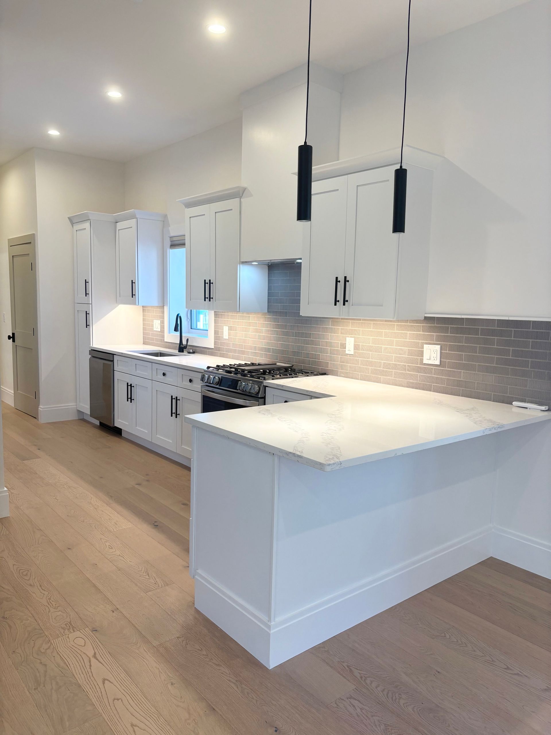 Modern white kitchen with light wood floors, countertops, and cabinets. Black light fixtures hang above.