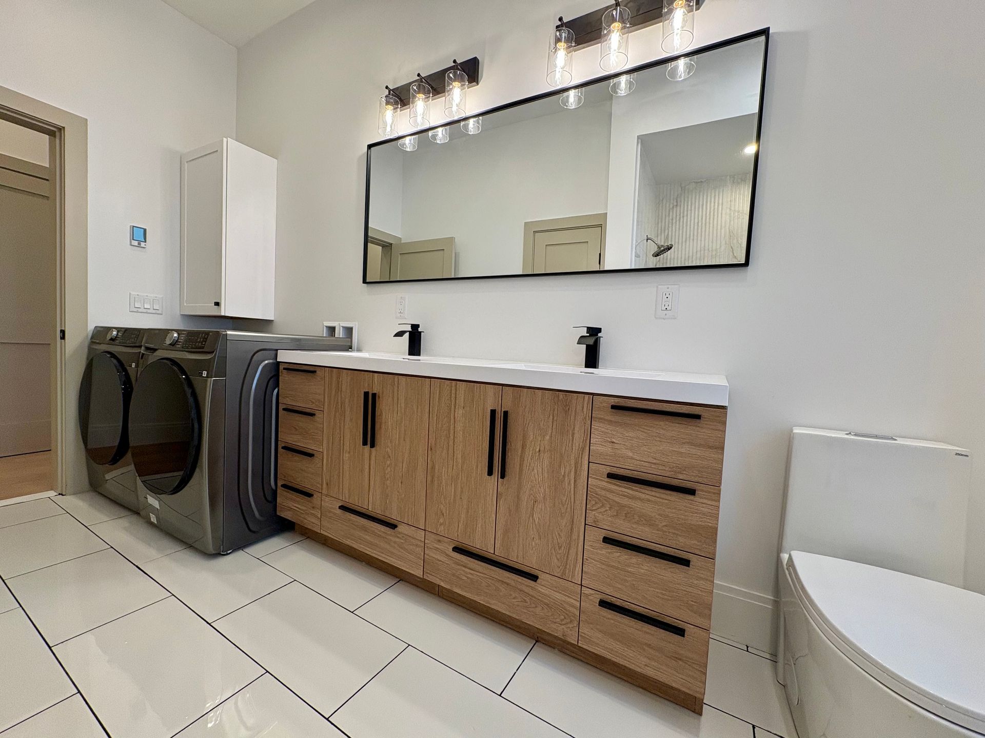 Modern bathroom with wooden vanity, double sinks, large mirror, and washer/dryer.