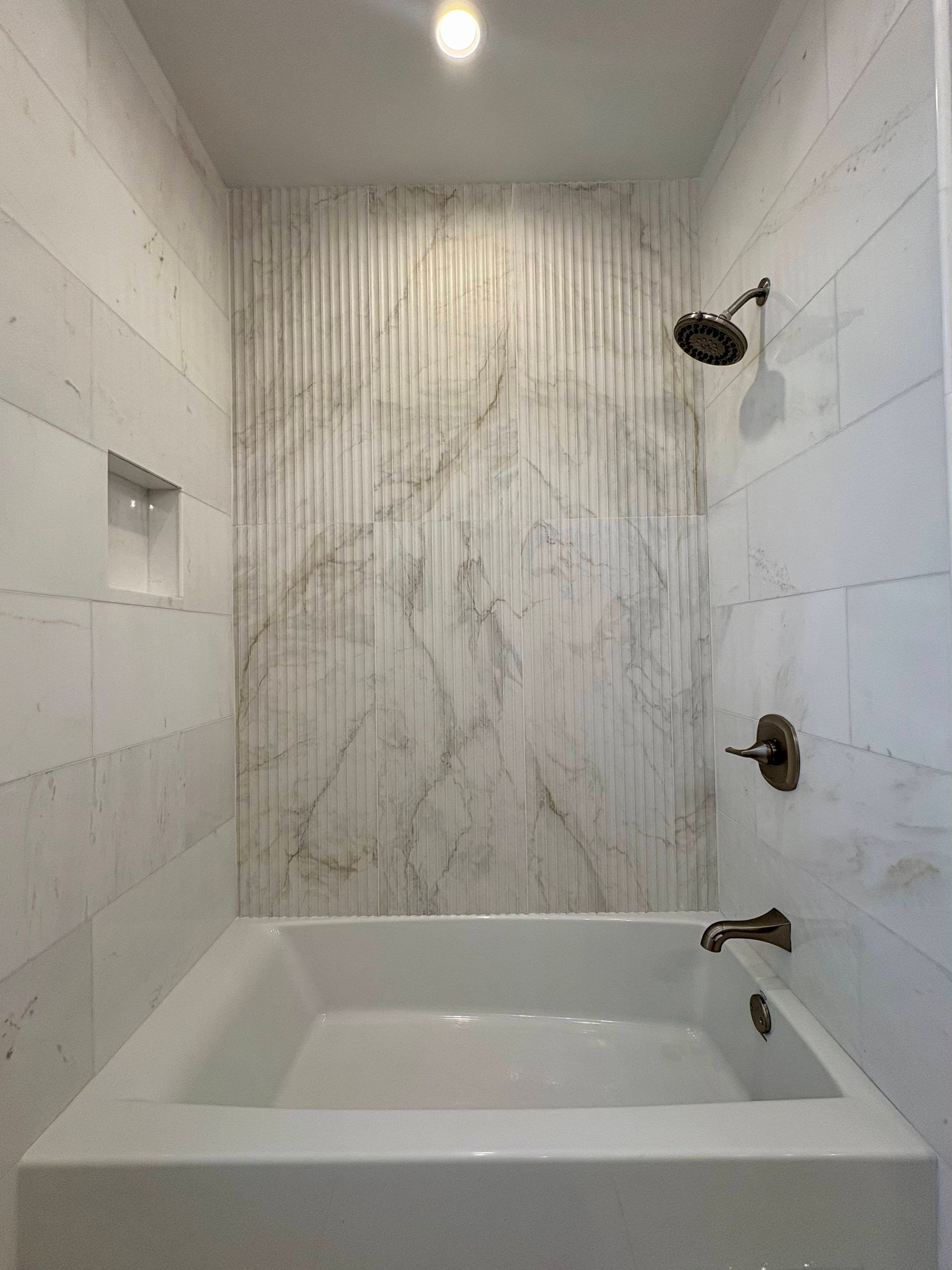 White tiled bathroom with a bathtub, showerhead, and a marble accent wall.