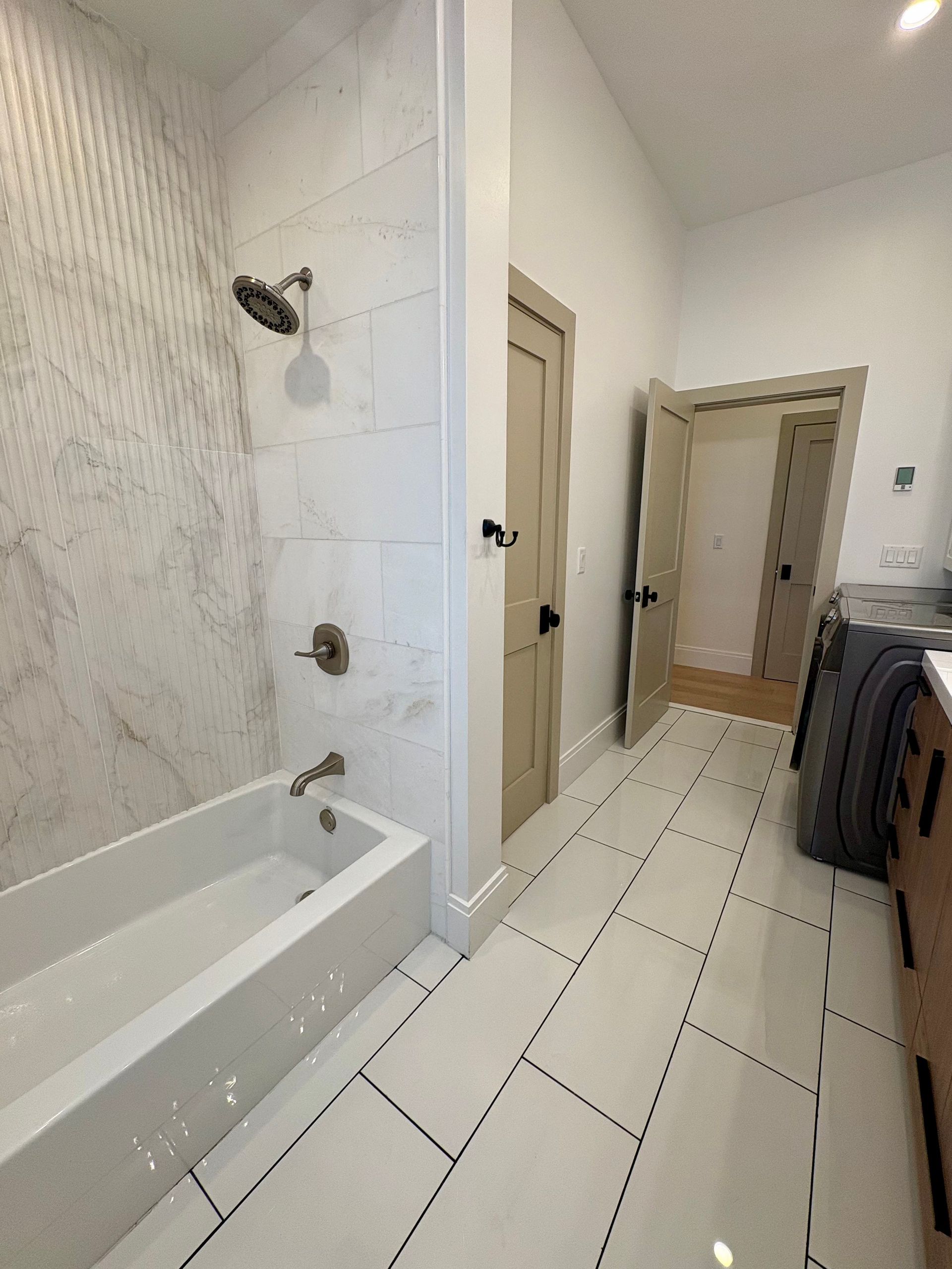 White bathroom with a tub, shower, and tile floor, alongside a doorway.