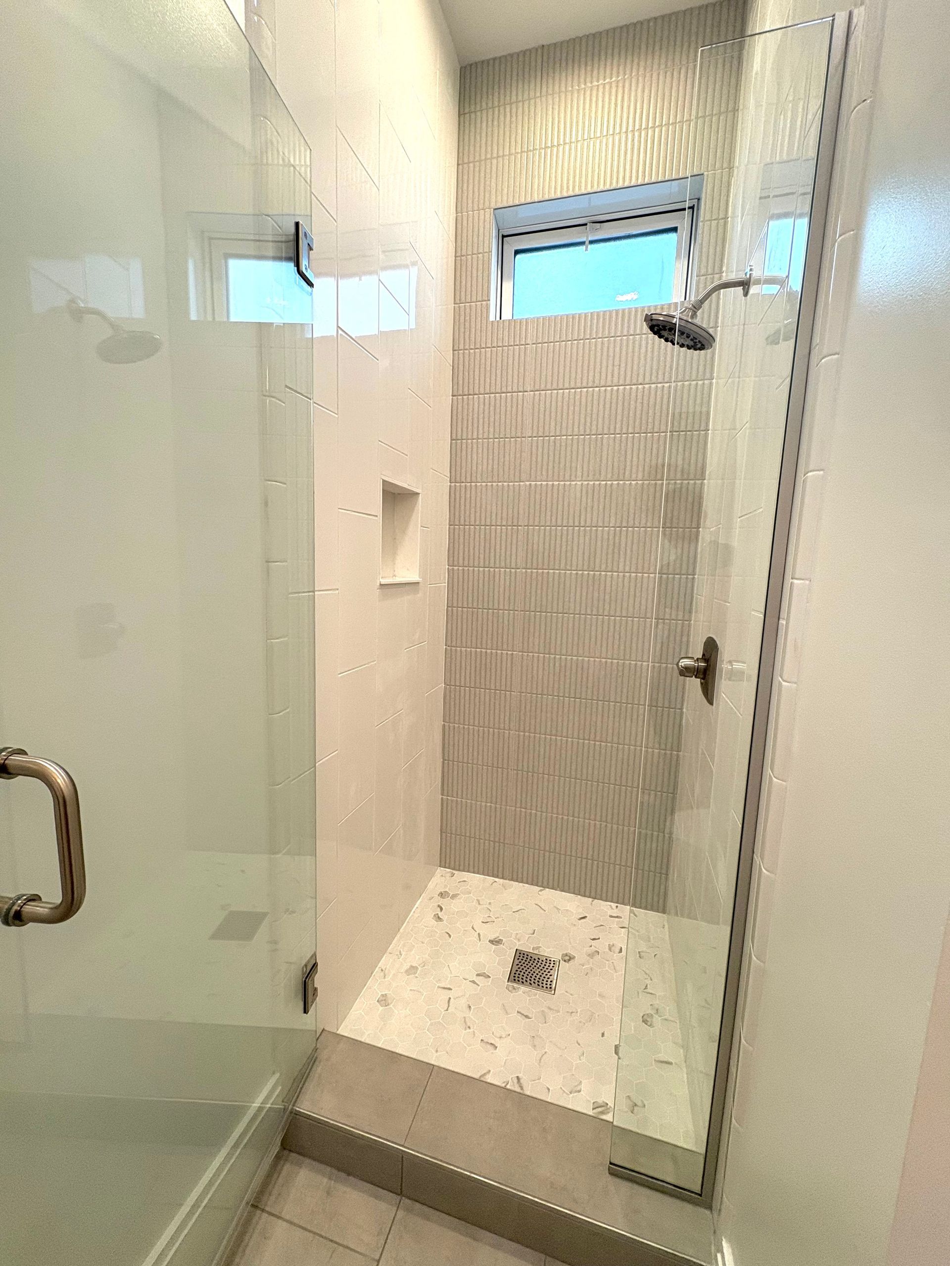 Shower stall with glass door and white tile walls and floor. Gold hardware.