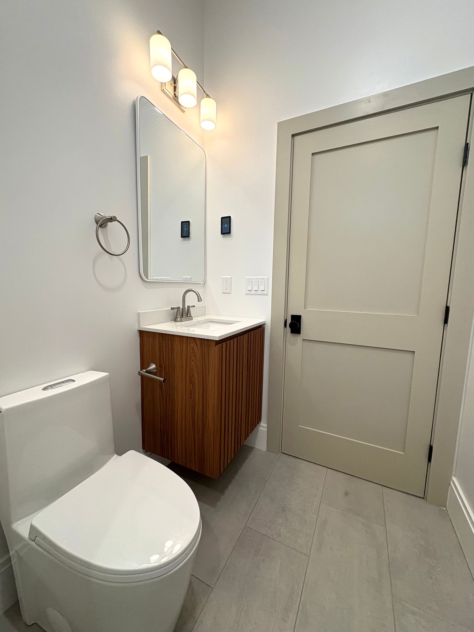 Modern bathroom with a white toilet, wooden vanity, and a rectangular mirror.