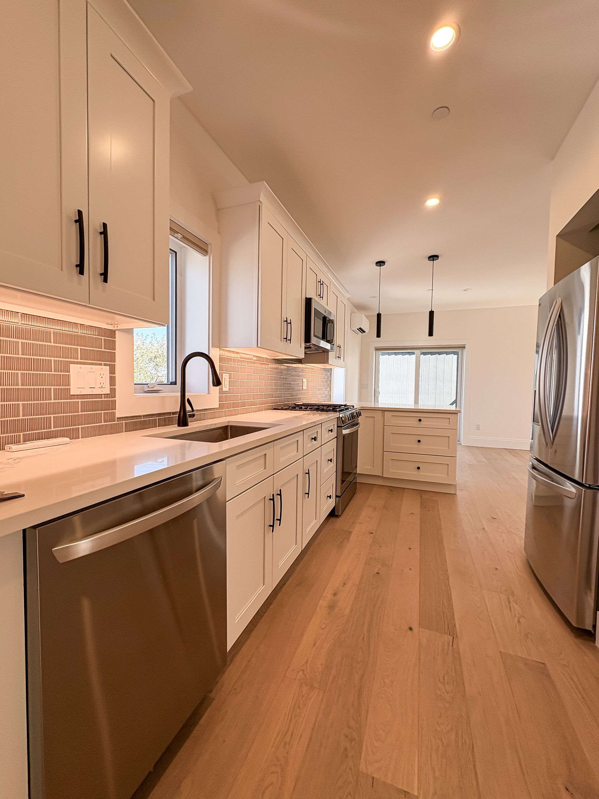 Modern kitchen with white cabinets, stainless steel appliances, and wood flooring.