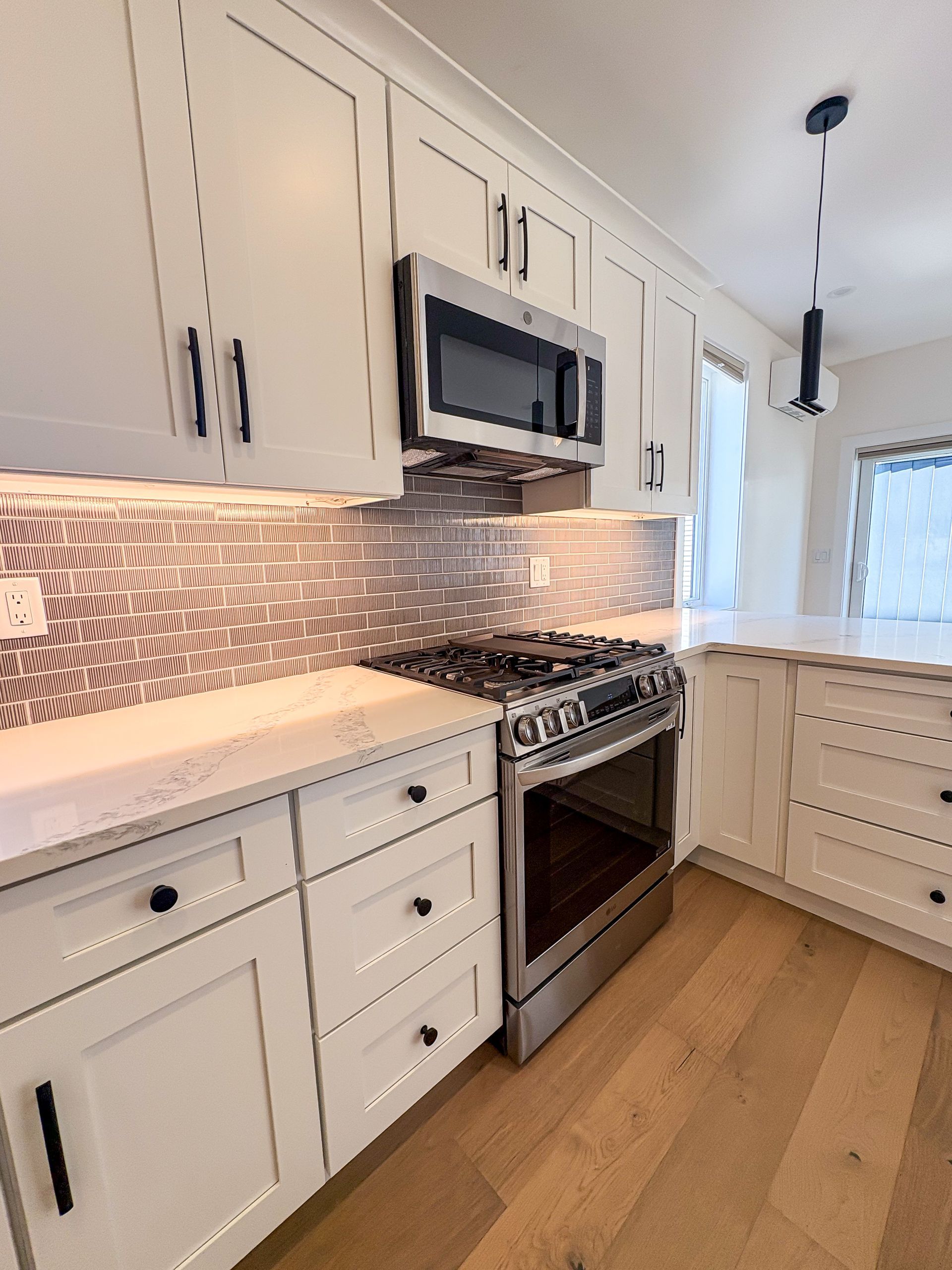 White kitchen with stainless steel appliances, mosaic backsplash, and light wood flooring.