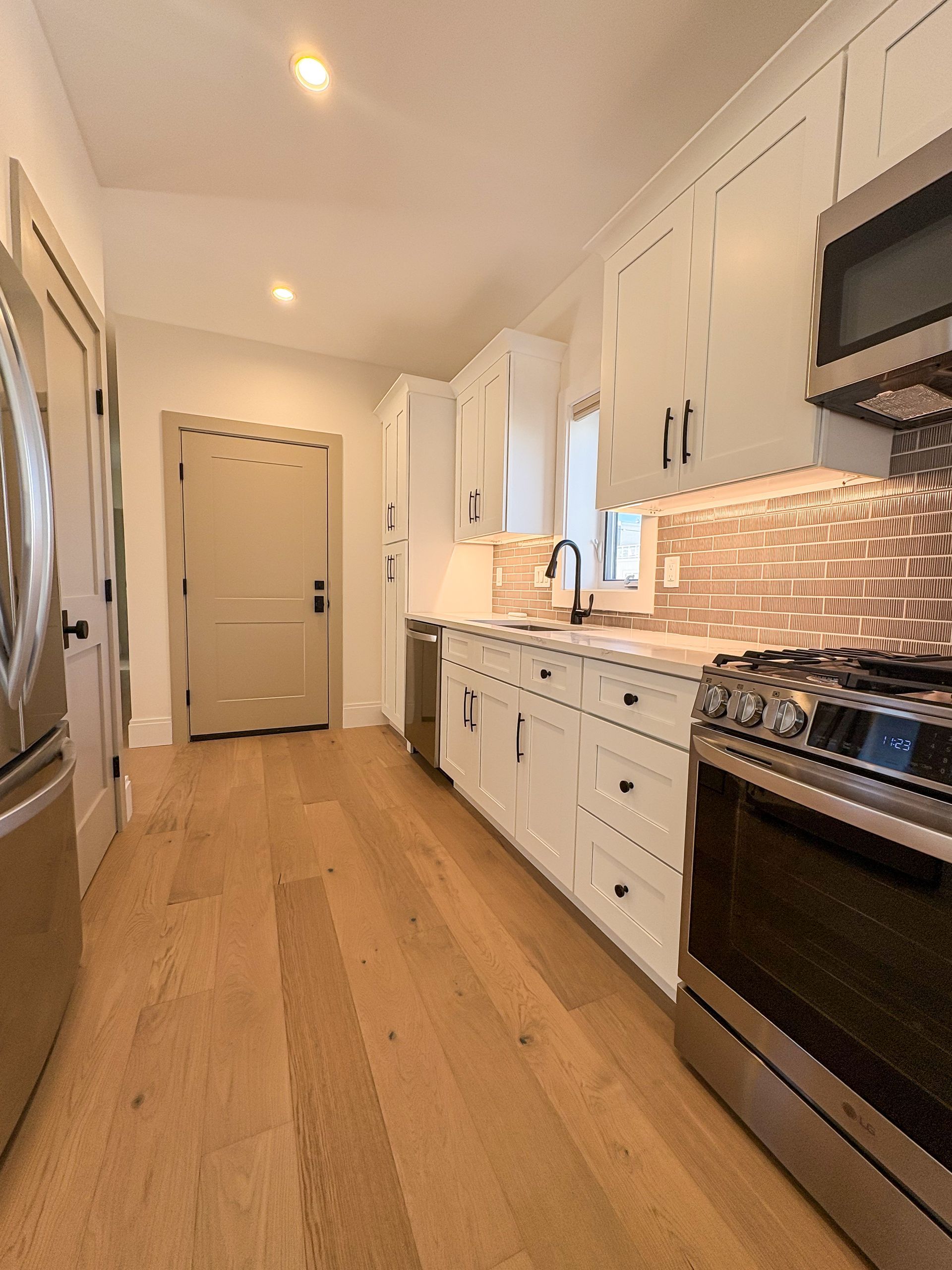 A bright kitchen with white cabinets, stainless steel appliances, and wood flooring.