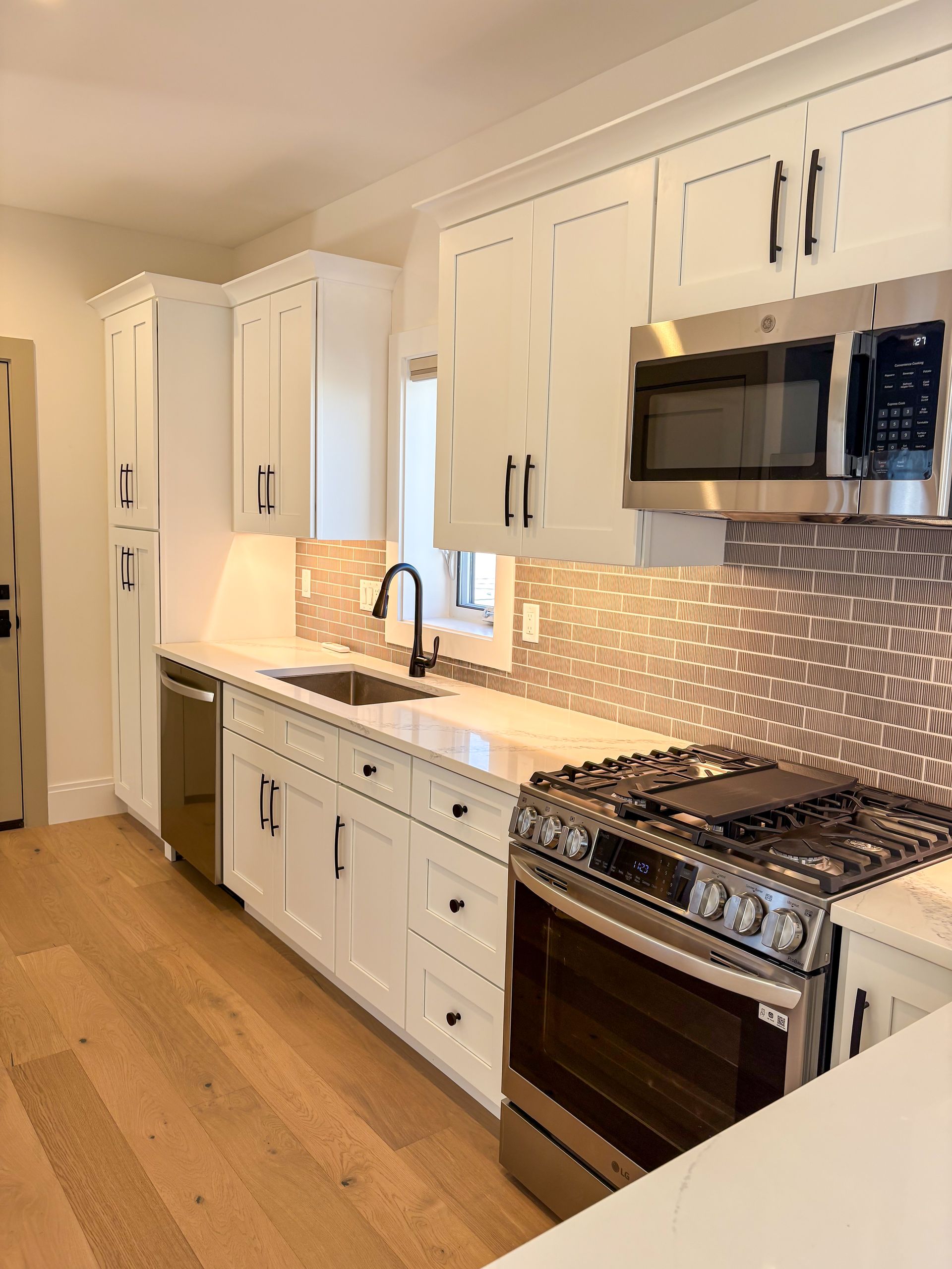 White kitchen with stainless steel appliances, dark hardware, and mosaic tile backsplash.