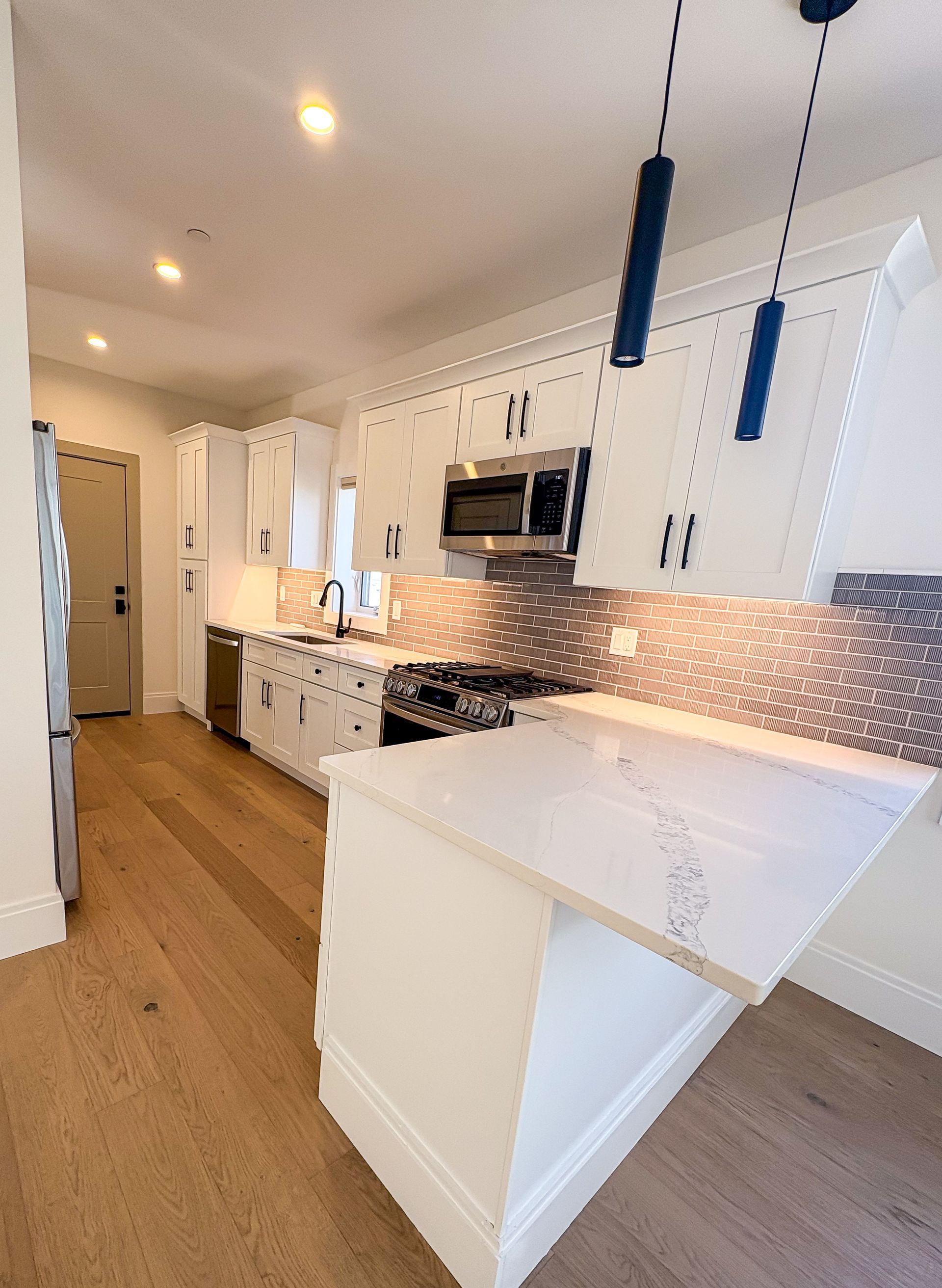 White kitchen with island, stainless steel appliances, wood floor.