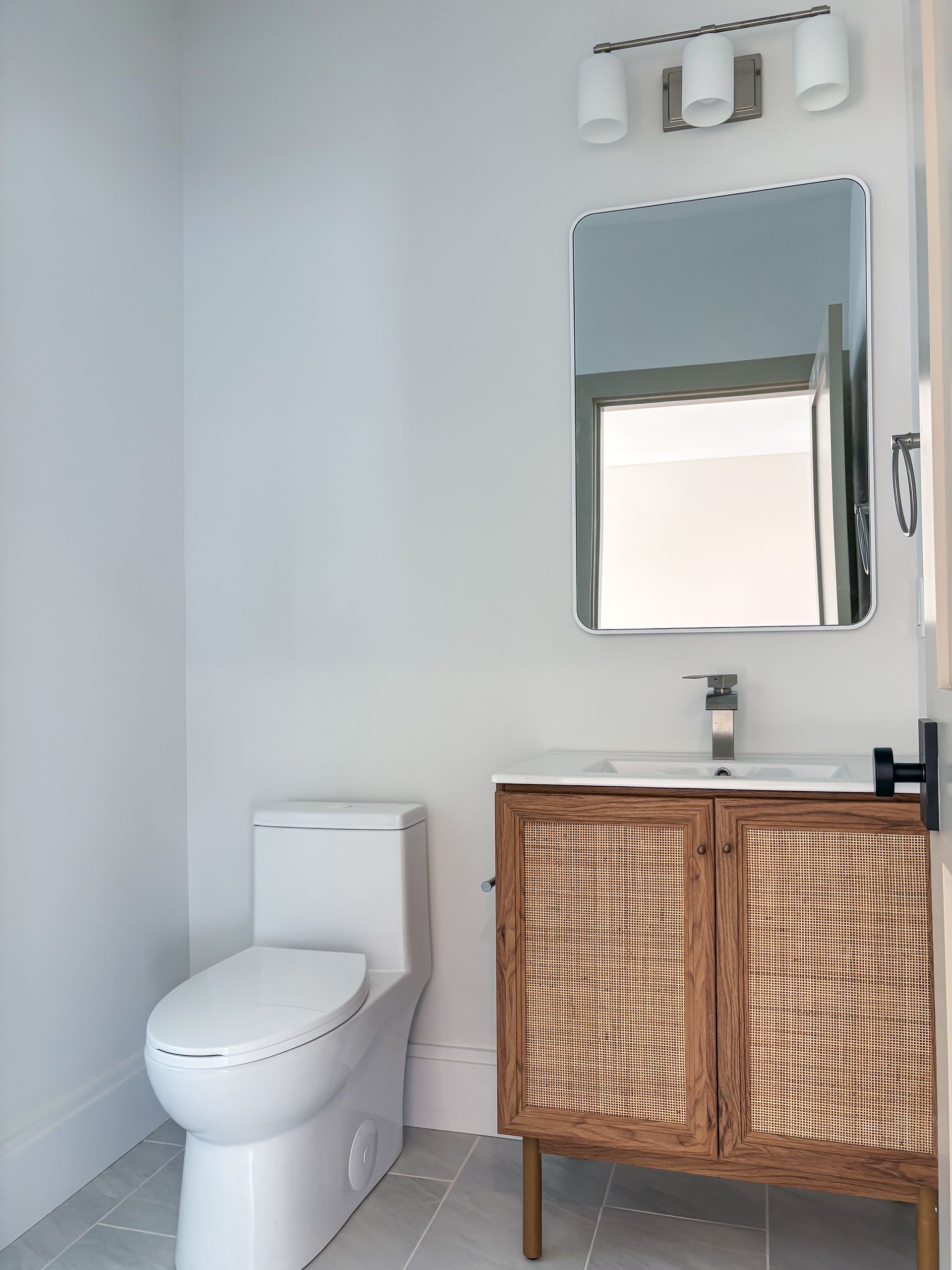 Bathroom with white walls, a toilet, a vanity with a woven door, and a mirror.