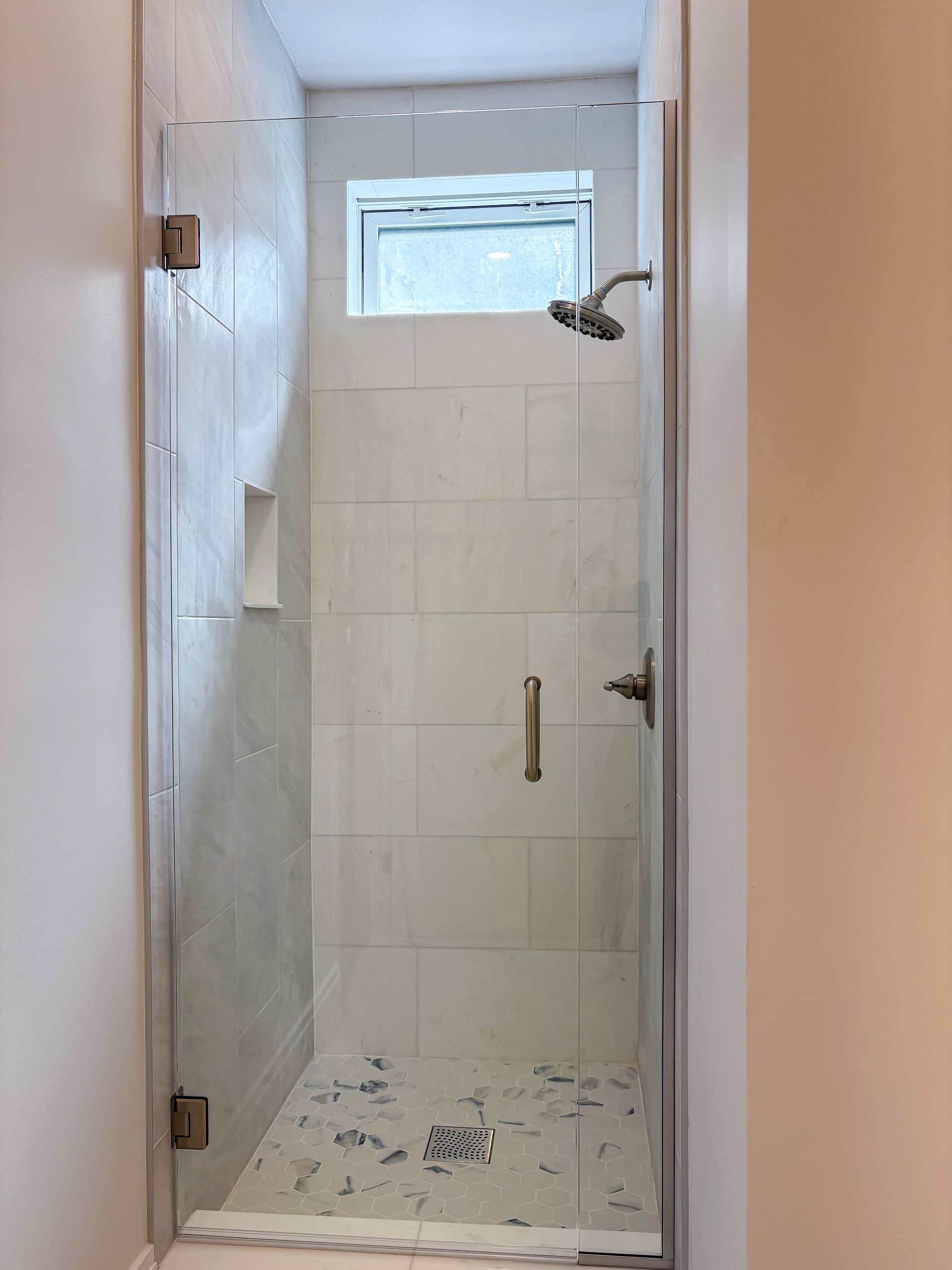 Glass shower enclosure with white tile walls and a small window.