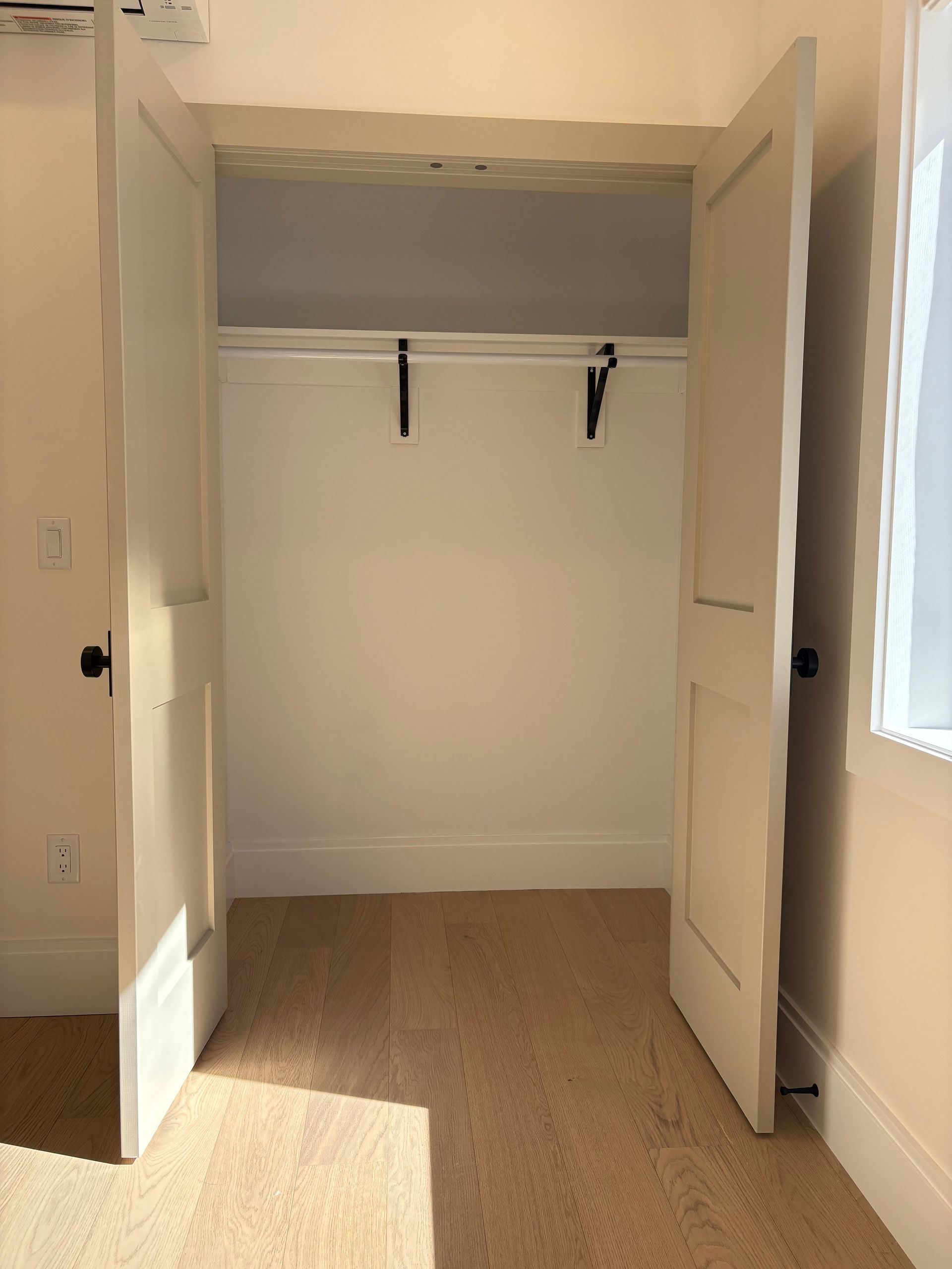 Empty white closet with open doors and clothing rod.