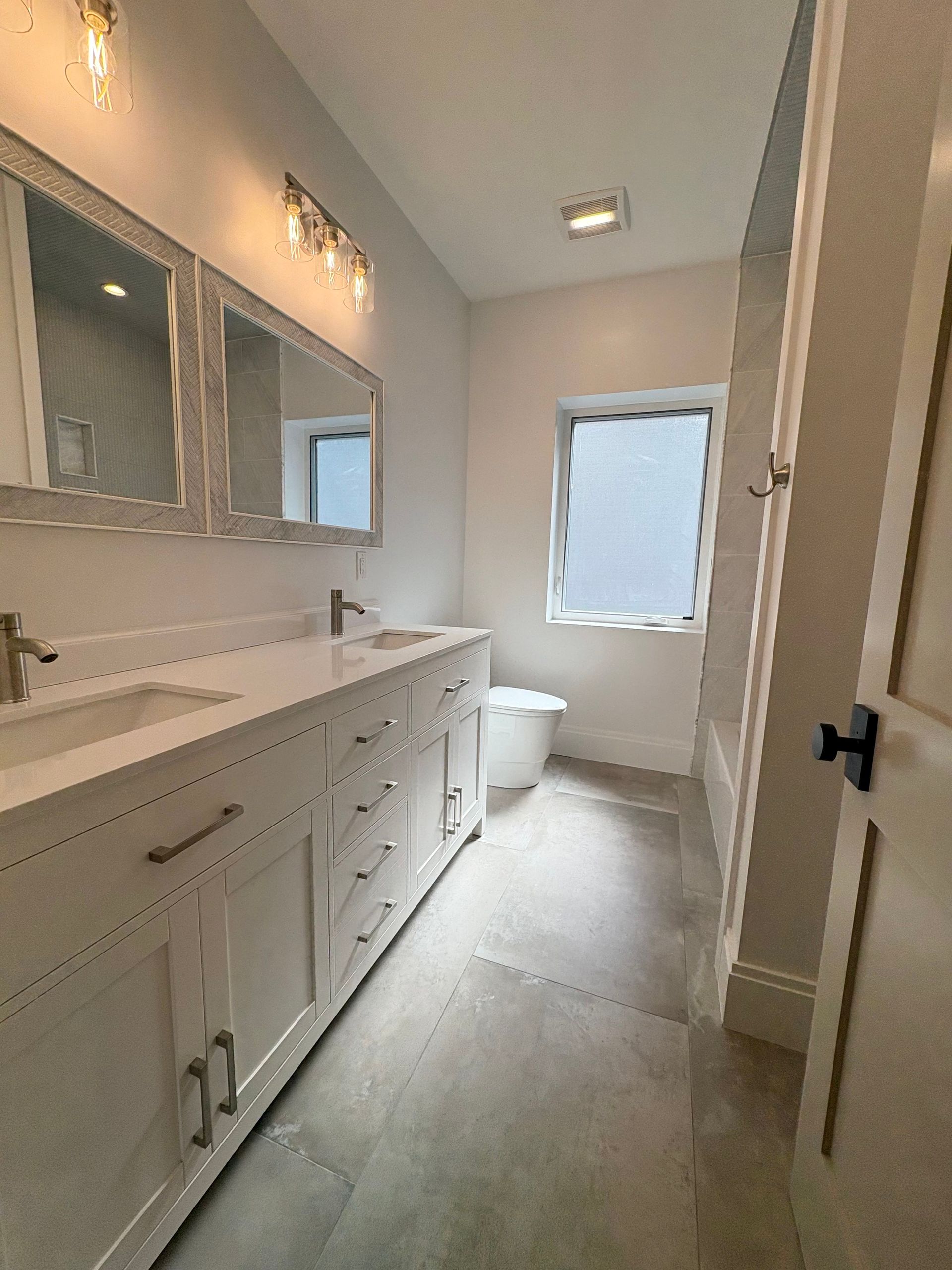 Bathroom with white cabinets, two sinks, mirrors, and a window.