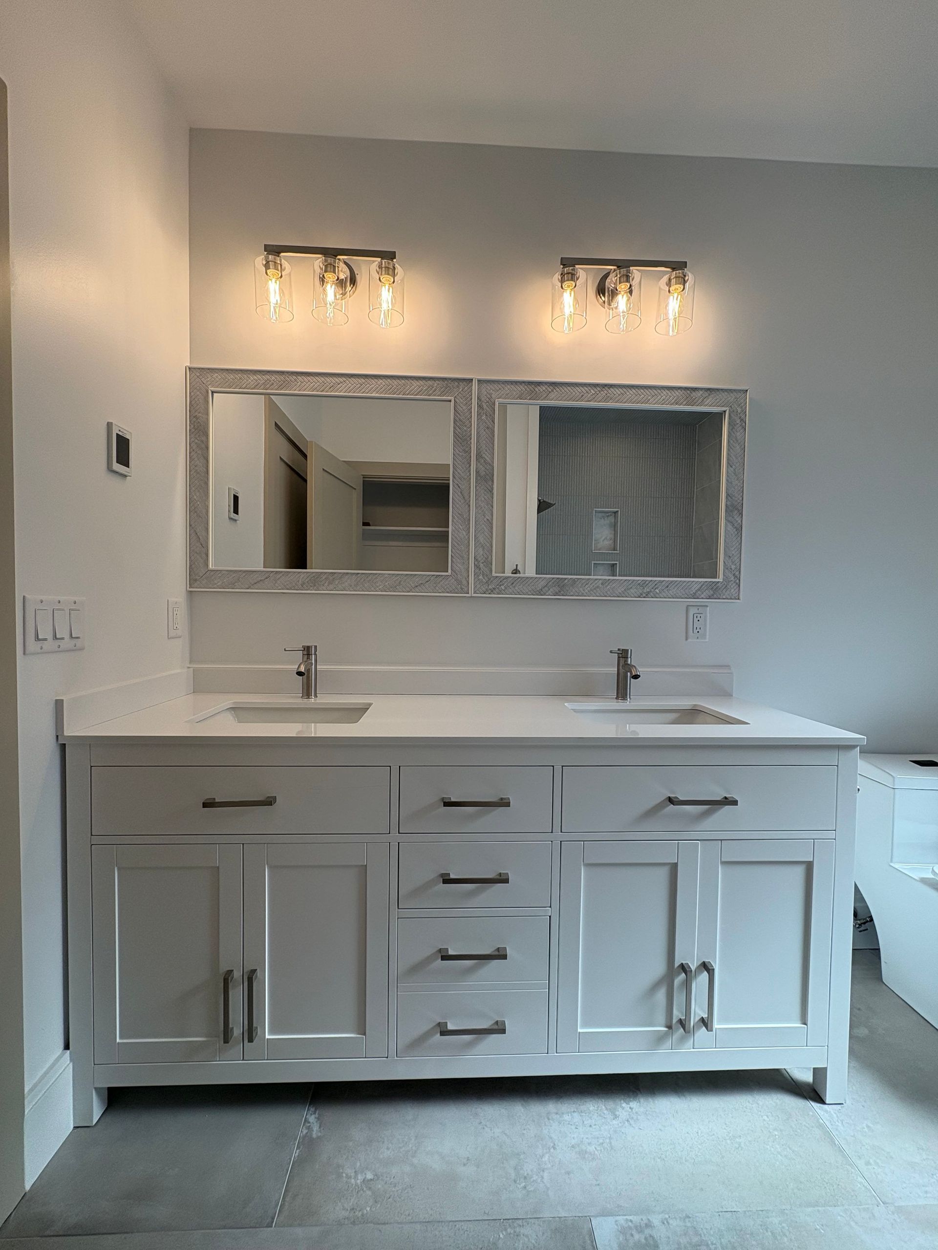 White double vanity with matching mirrors and light fixtures in a bathroom.