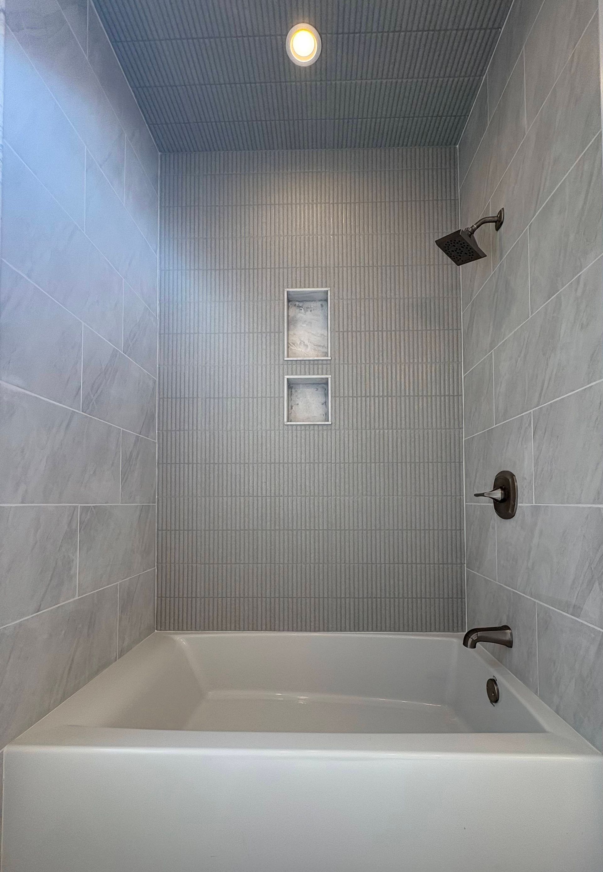 Gray-tiled bathroom with a bathtub, showerhead, and two built-in shelves.