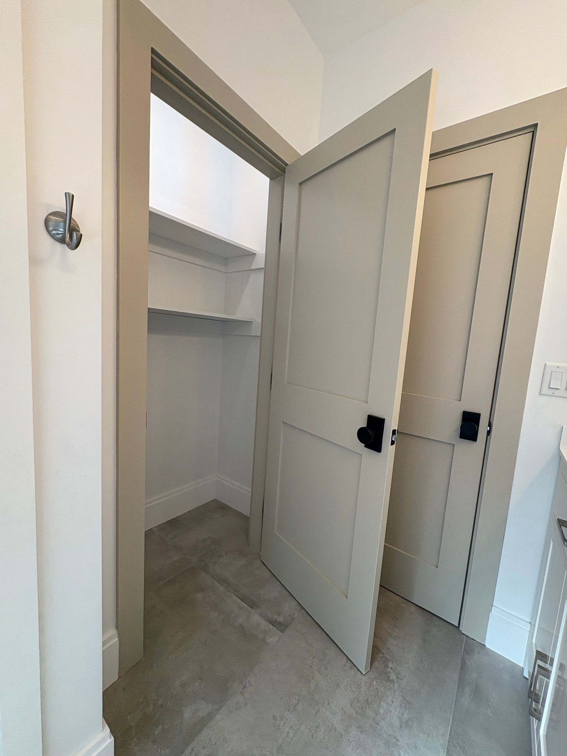 Closet with partially open door, shelves, and beige frame, in room with carpet and a closed door.