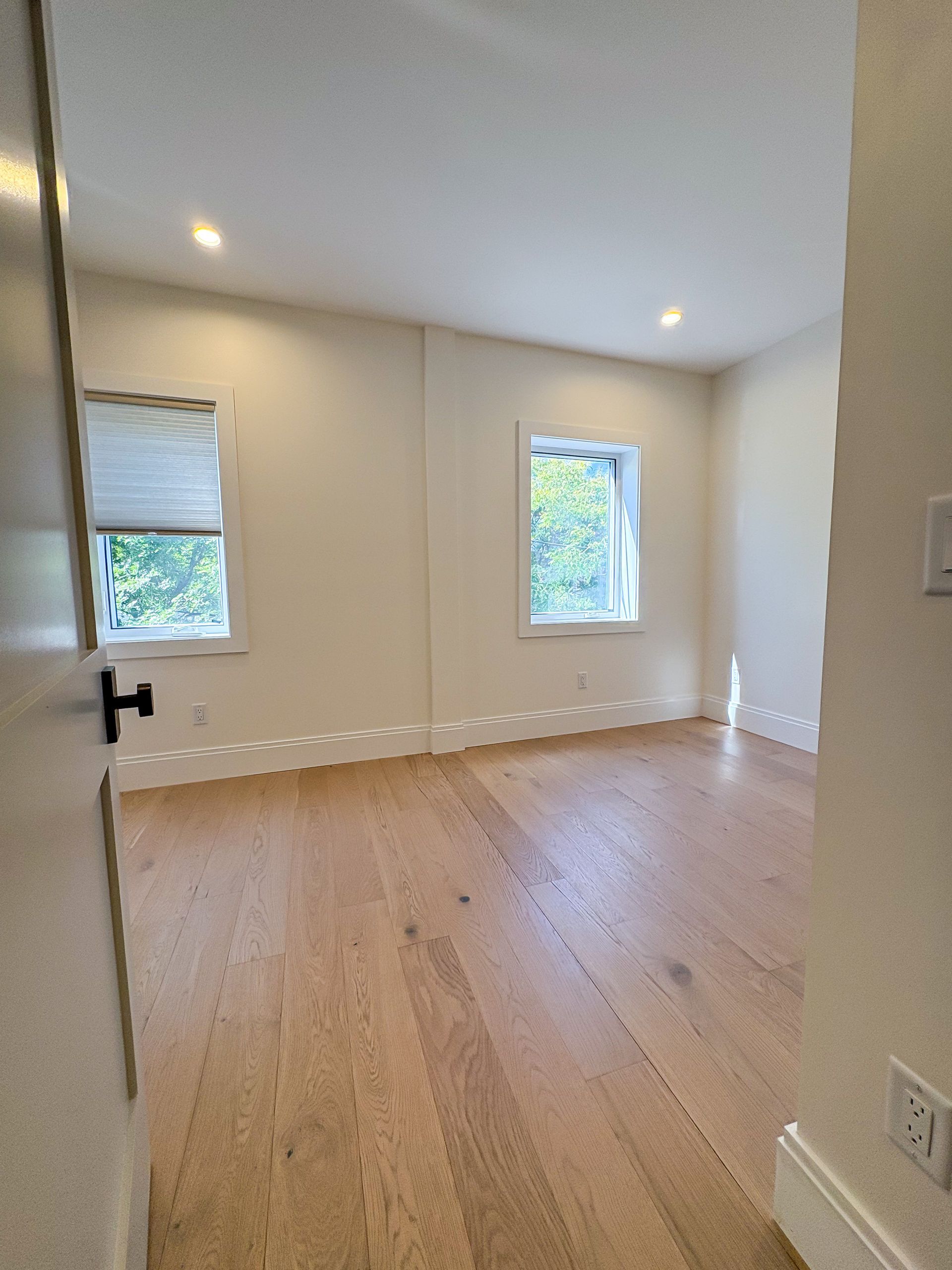 Empty room with wood floor, two windows, and recessed lighting.