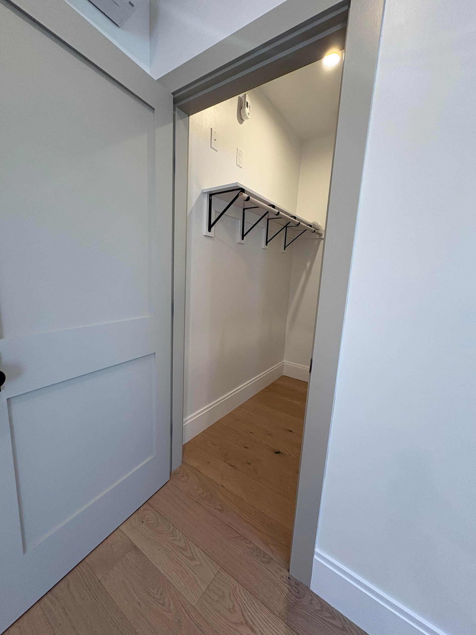 Open doorway to a small closet with shelves and hardwood floor. Door is white.