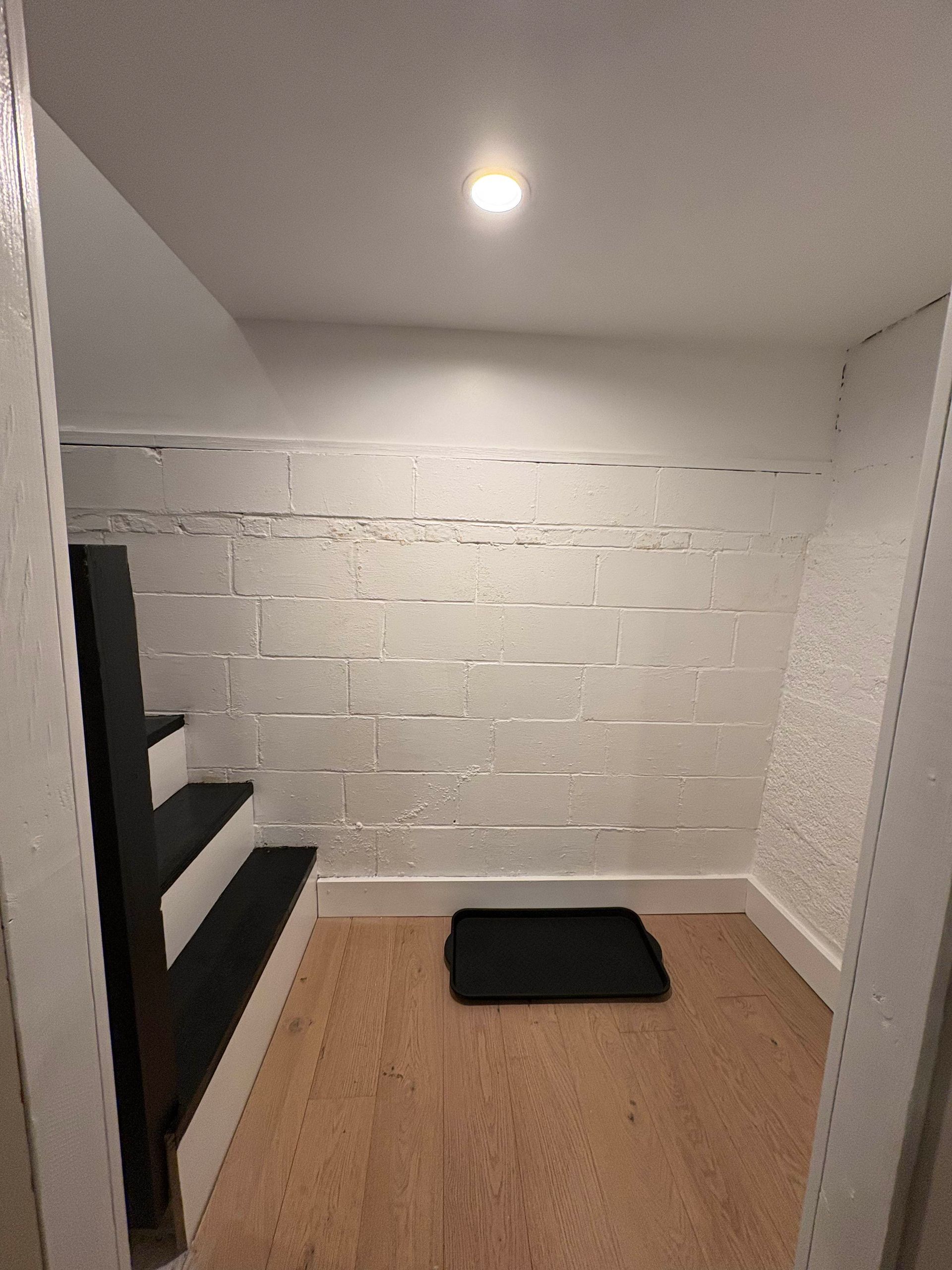 Small room with stairs, white block walls, wood floor, and a black mat.