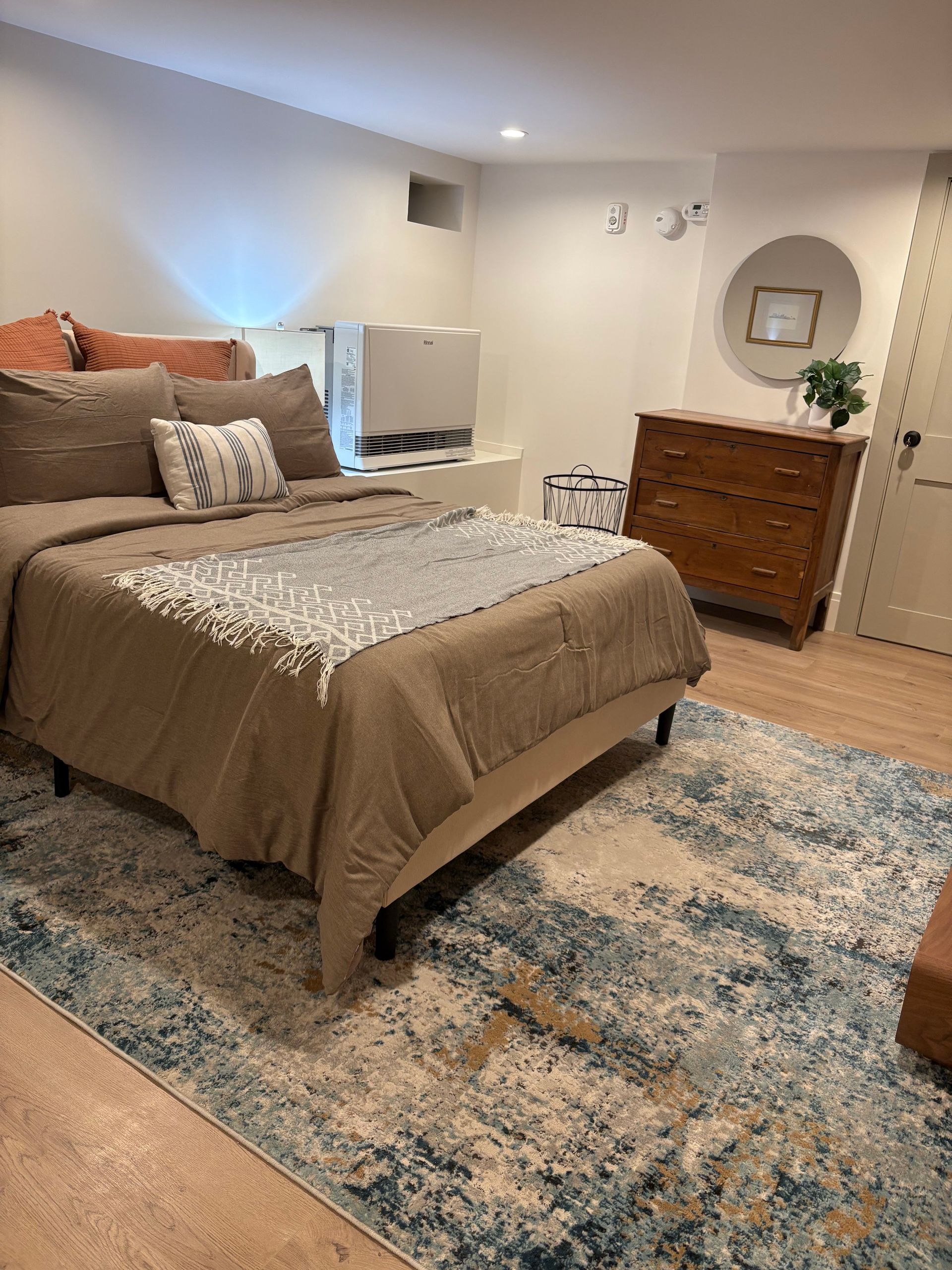 Bedroom with bed, dresser, and patterned rug. Warm beige and blue color scheme.