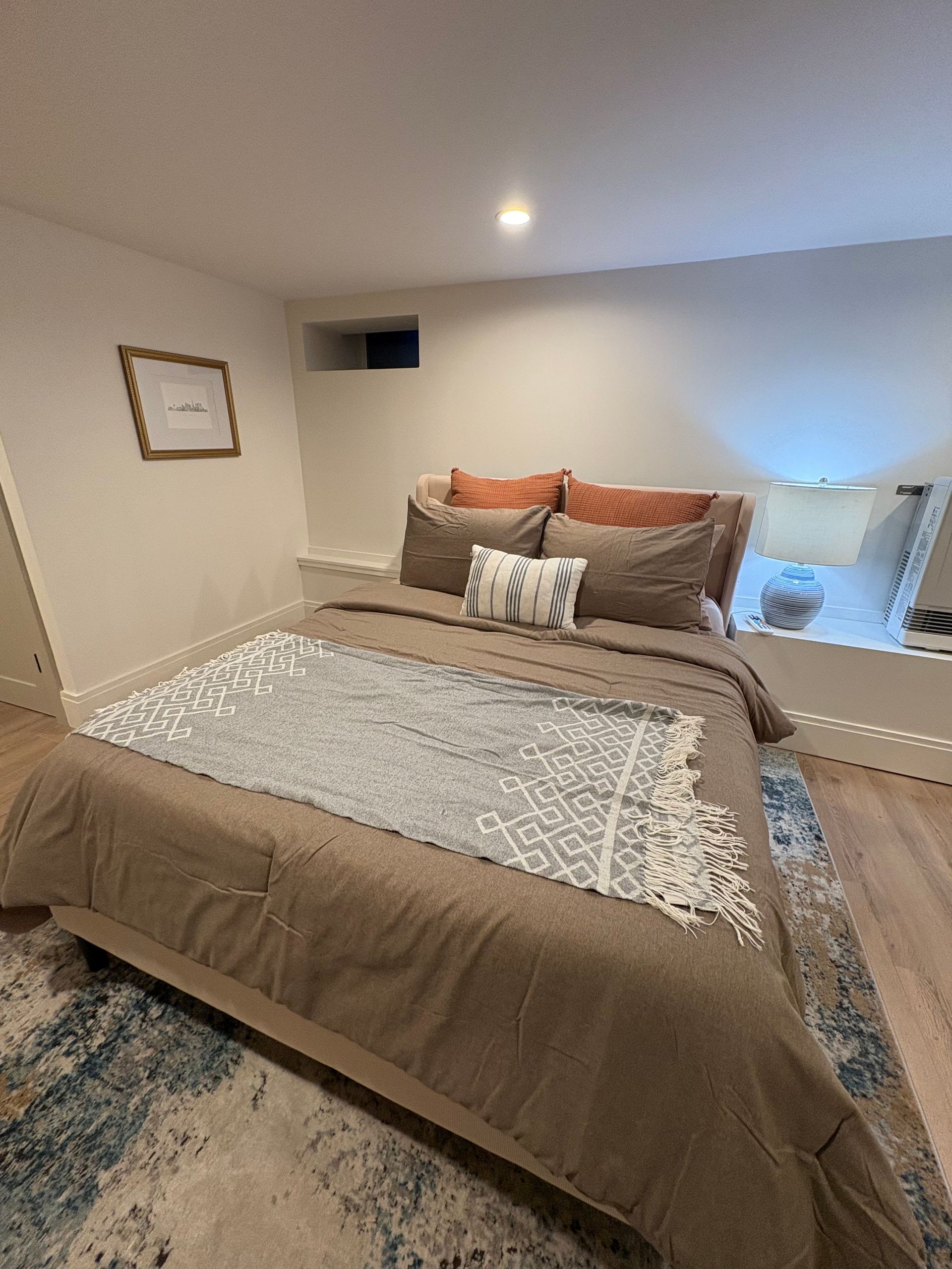 Bedroom with bed, brown bedding, decorative pillows, rug, and framed artwork.