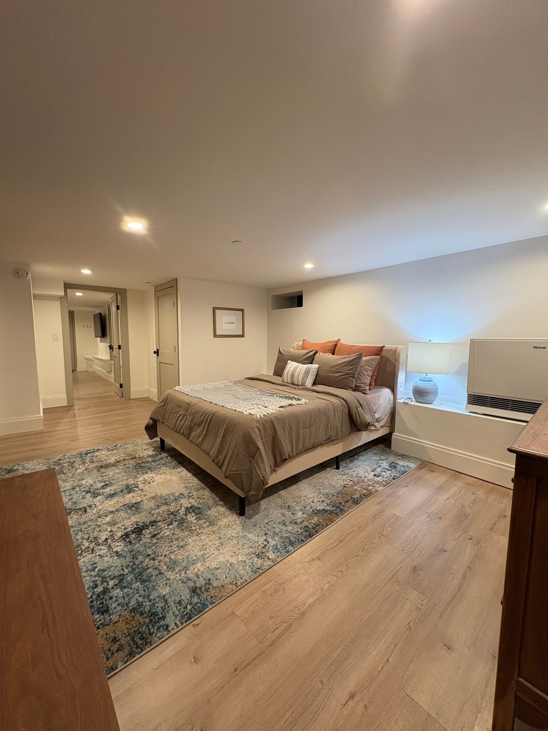 Bedroom with bed, rug, and dresser. Light-colored walls and flooring.