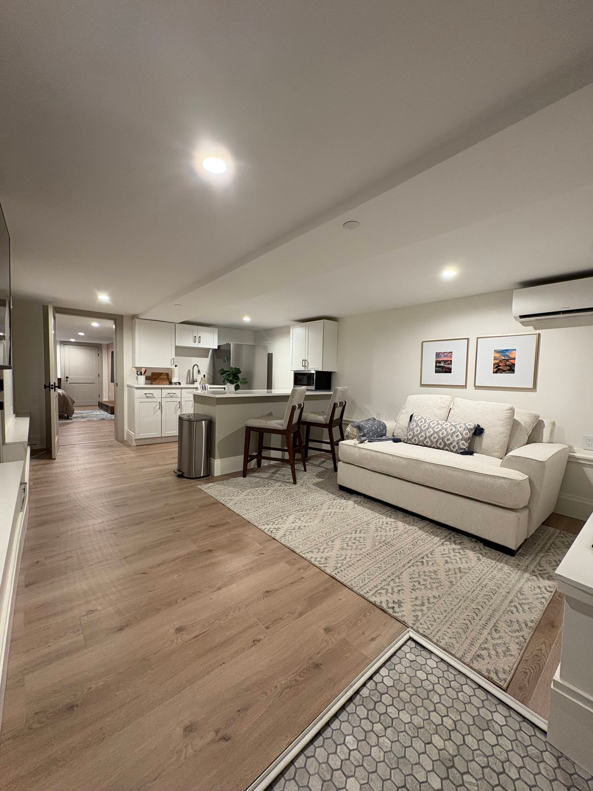 Spacious, modern living space with kitchen, dining area, and white sofa on a rug, light wood floors.