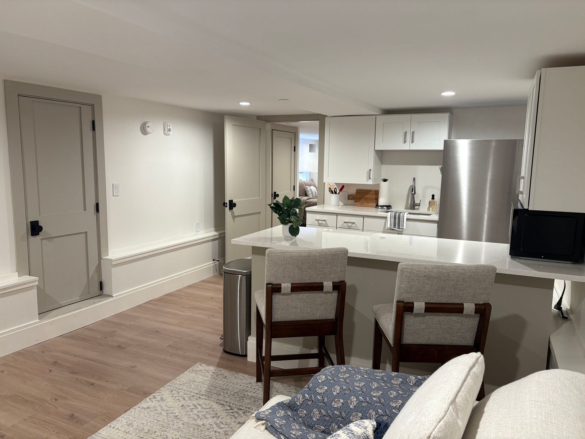 Open-concept kitchen with white cabinets, island with stools, stainless steel fridge, and door.