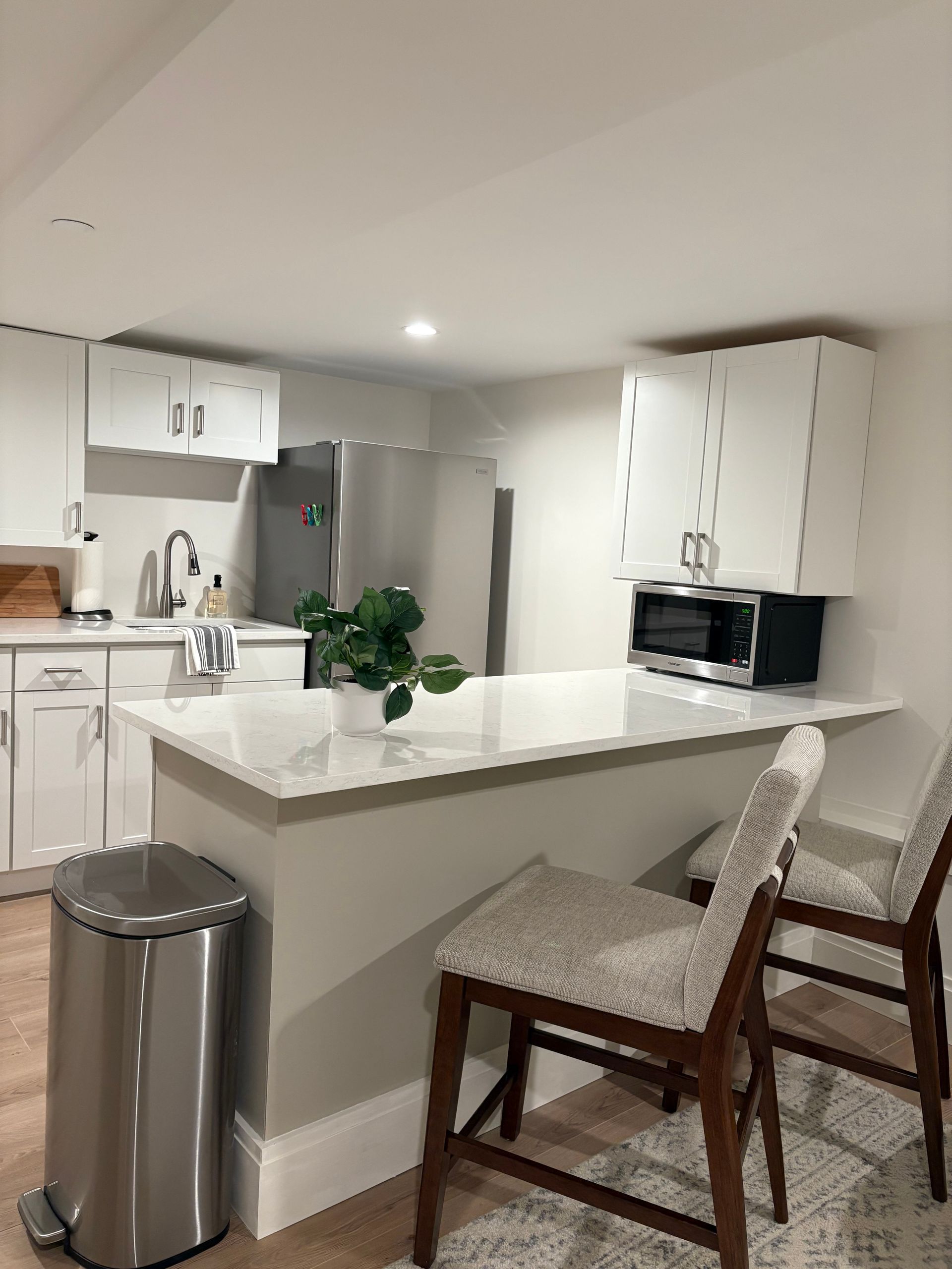 Modern kitchen with white cabinets, stainless steel appliances, and a countertop with two barstools.