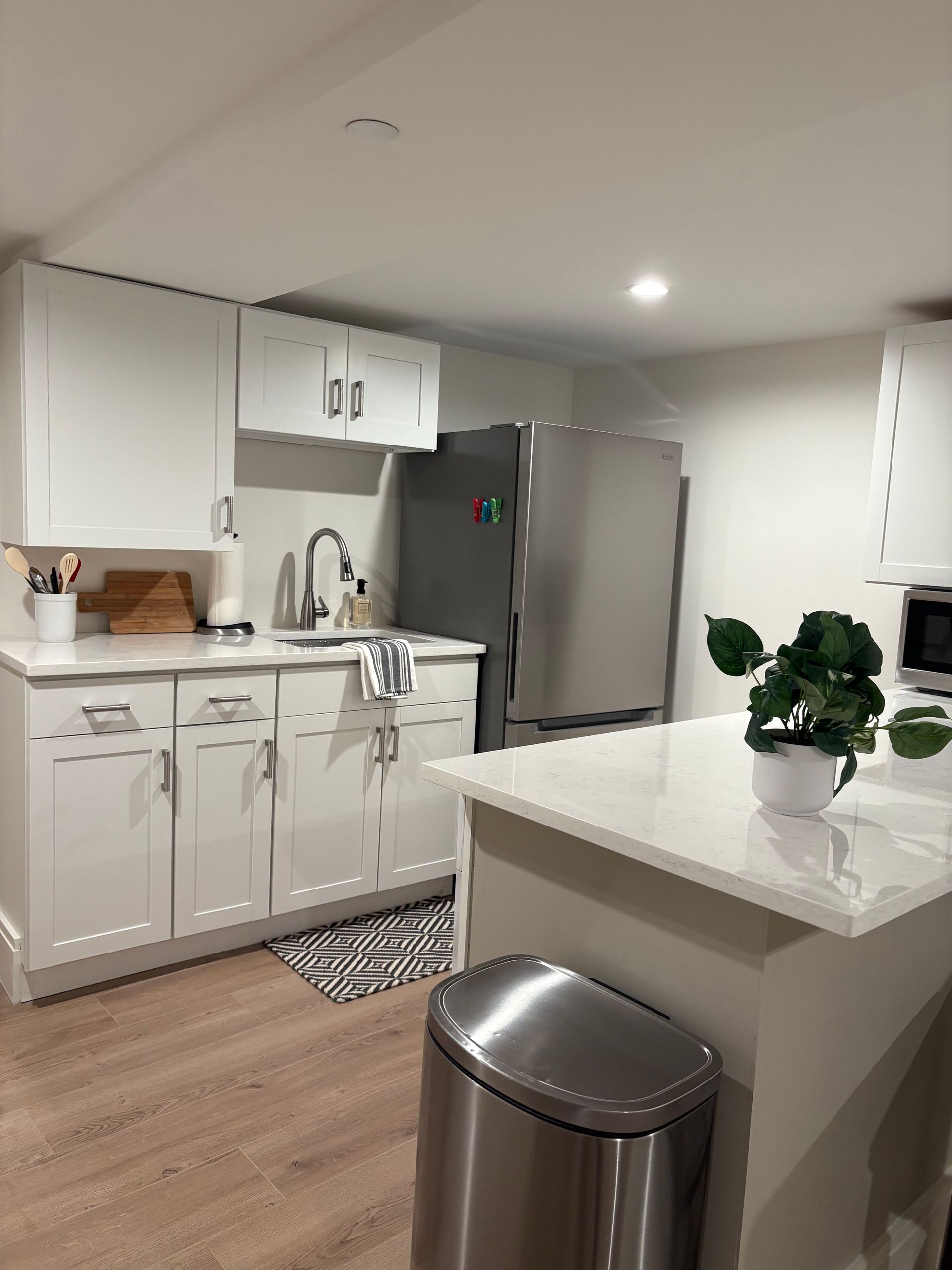 White kitchen with cabinets, stainless steel refrigerator, and island with a plant.