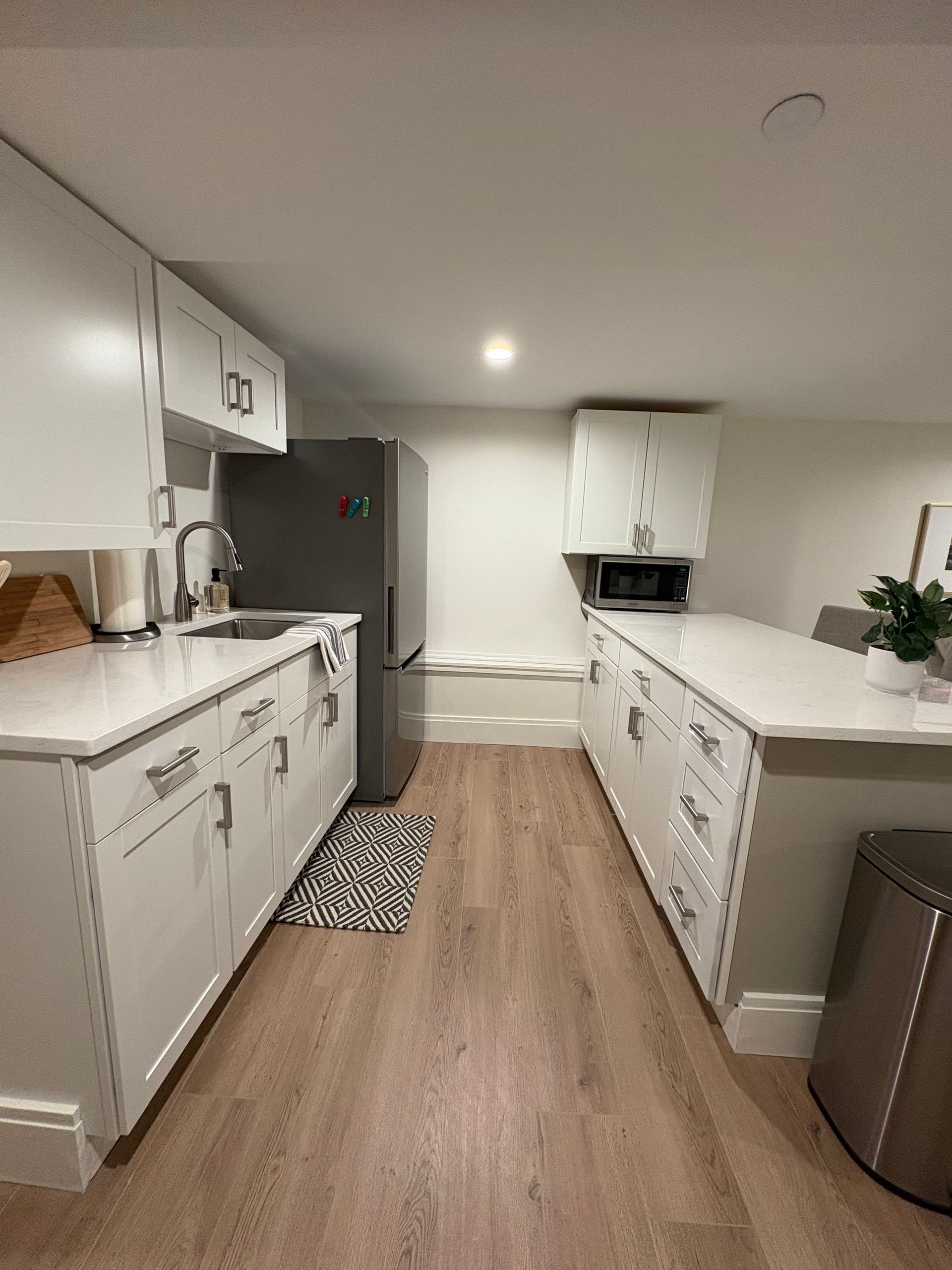 White kitchen with stainless steel refrigerator, white cabinets, and island with countertop.