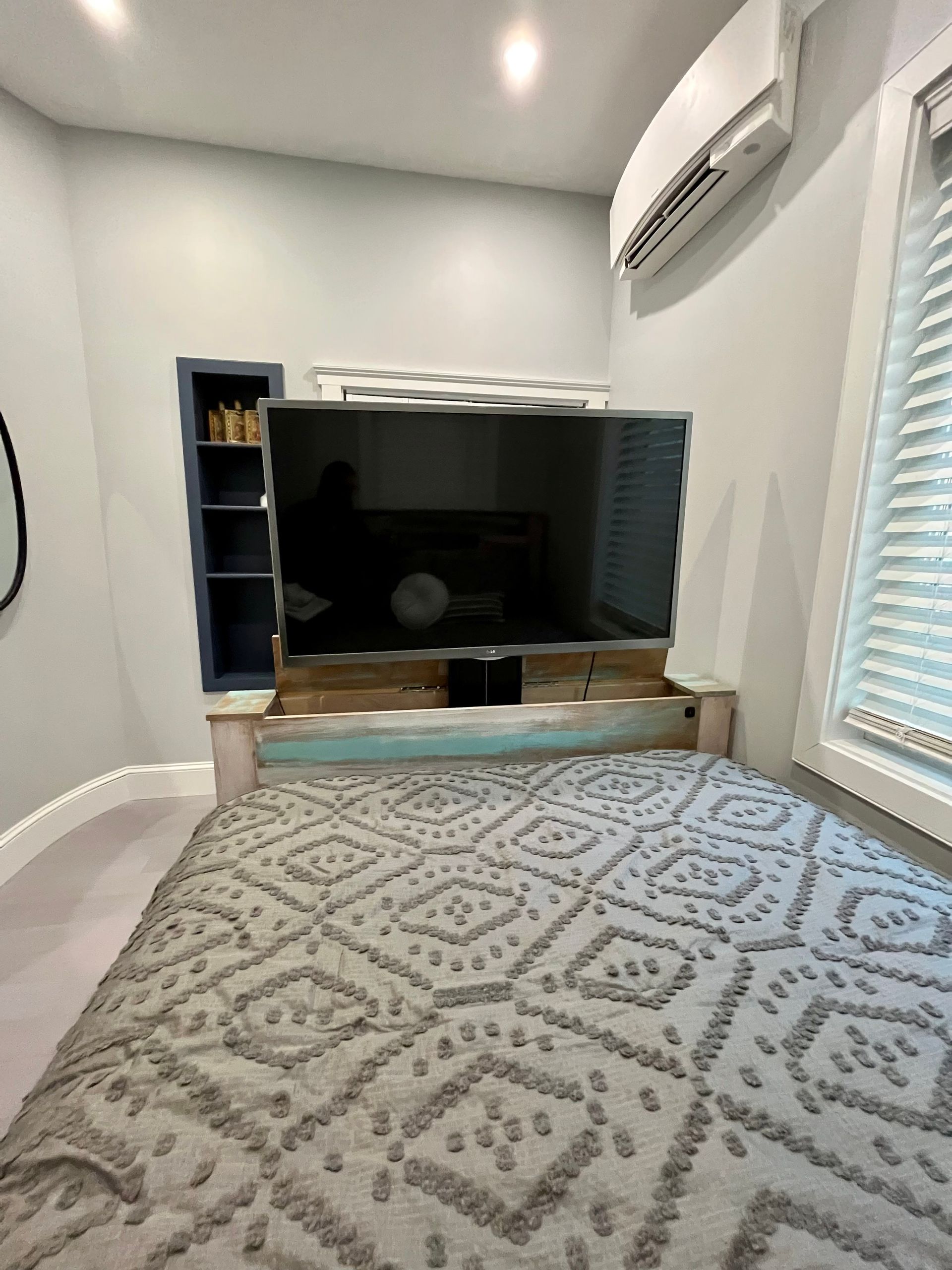 Bedroom with large TV mounted on headboard. Blue and turquoise distressed wood. Gray patterned quilt.