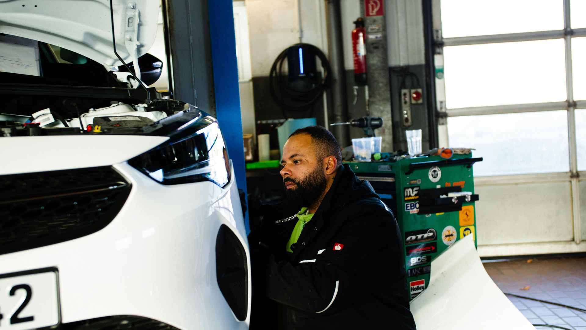 Mechanic in a garage, inspecting the front of a white car.