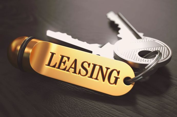 Penna dorata con la scritta “LEASING” e due chiavi argentate su una superficie scura