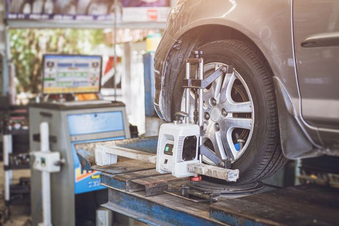 Ruota di un'auto su una macchina per l'allineamento in un'officina meccanica, con monitor del computer nelle vicinanze.