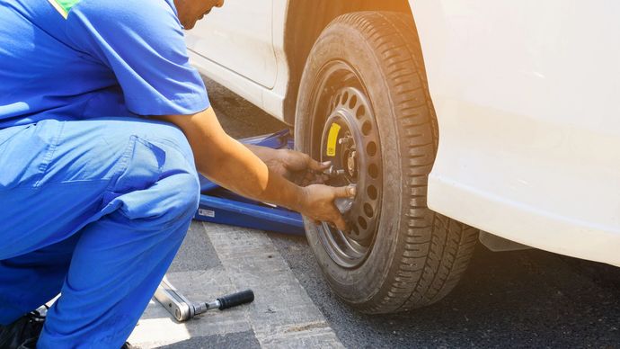 Un meccanico in tuta blu stringe una ruota di un'auto bianca con una chiave inglese.