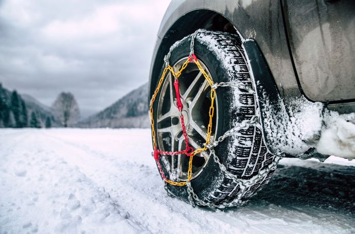 Pneumatico di un'auto equipaggiato con catene da neve rosse e gialle che percorre una strada innevata.