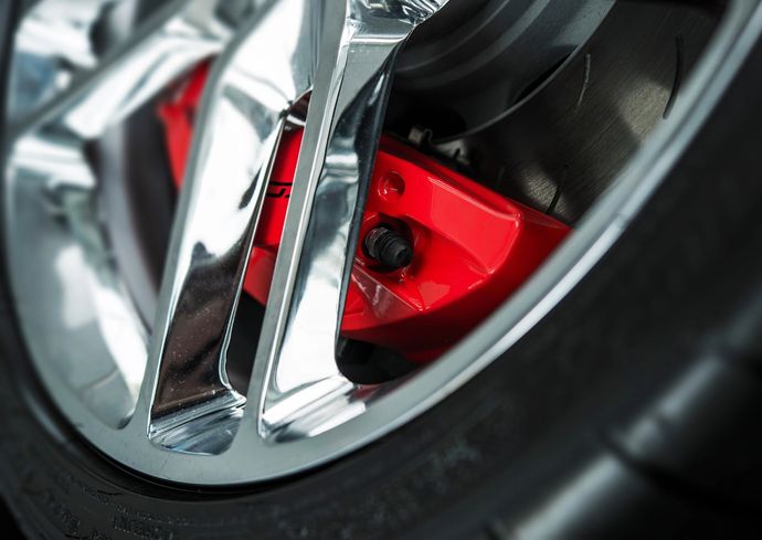 Primo piano di un cerchione per auto con raggi cromati e pinza freno rosso brillante.