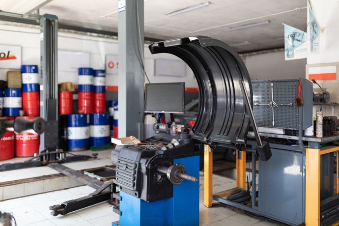 Officina industriale con un macchinario nero curvo, armadietti blu e barili rossi e blu impilati.