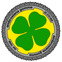 Logo di pneumatico giallo e grigio con un quadrifoglio verde e la scritta curva nera 
