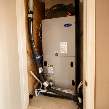 Utility closet with a gray HVAC unit and exposed pipes in a cramped indoor alcove