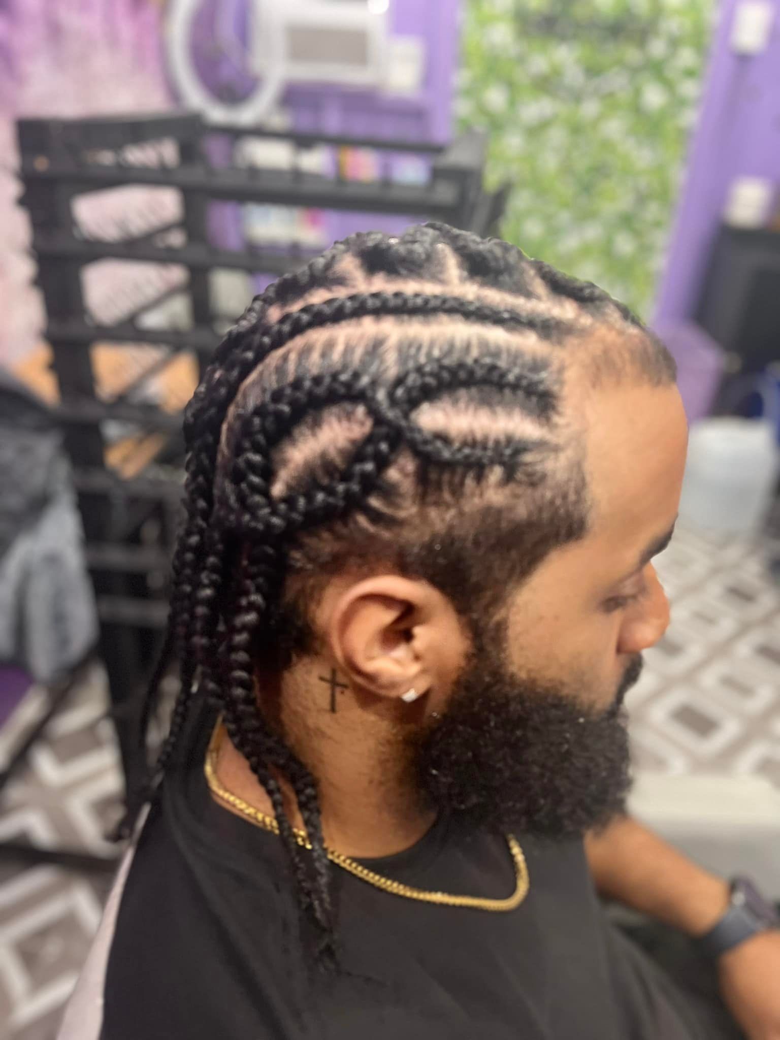 Man with cornrow braids and beard, wearing gold chain.