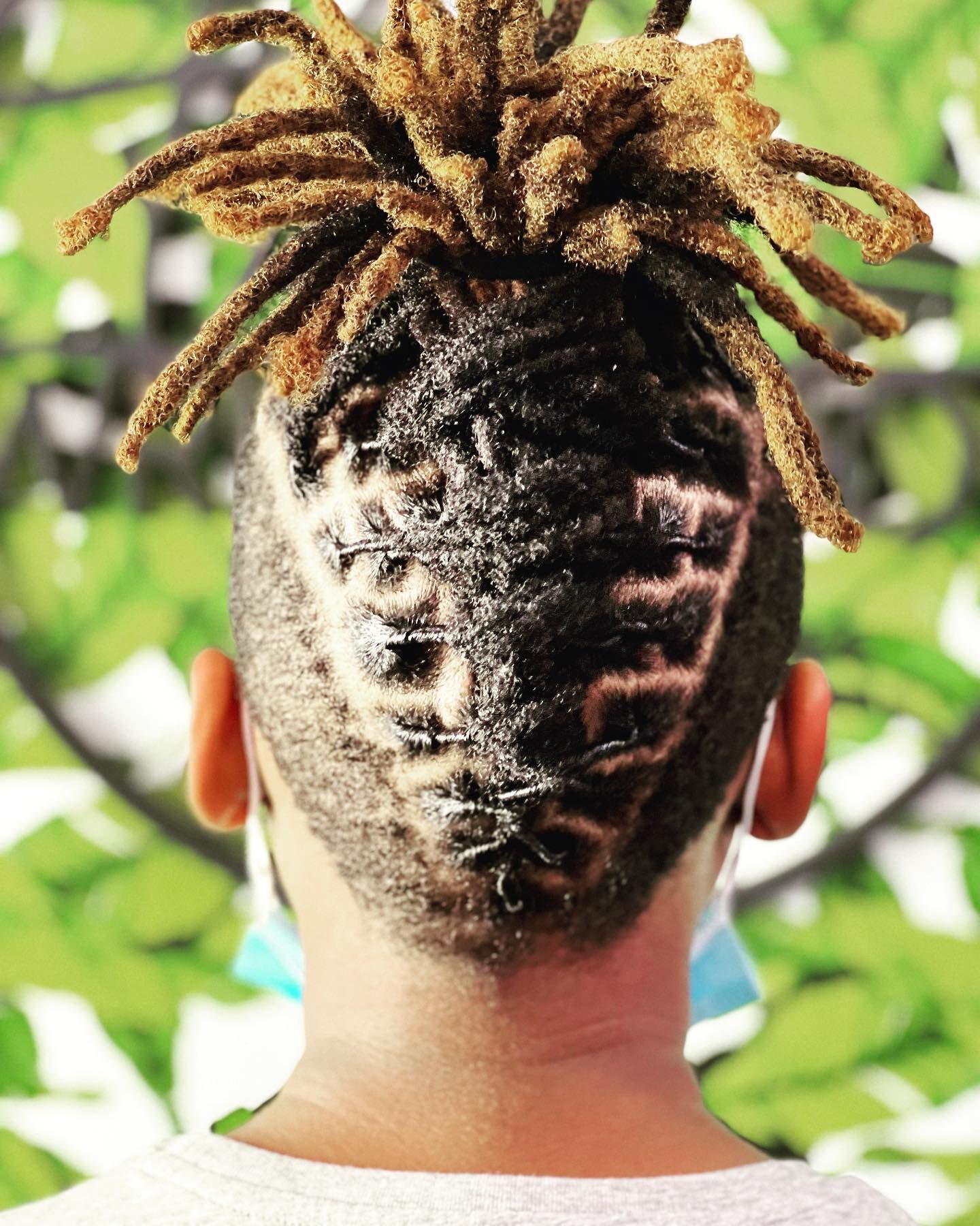 Person with shaved design on the back of their head with dreadlocks in a bun. Light green background.