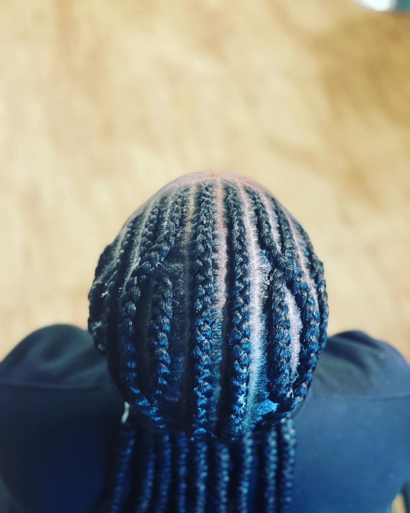 Overhead view of a person's head with rows of neatly braided hair, visible scalp, and a dark blue top.