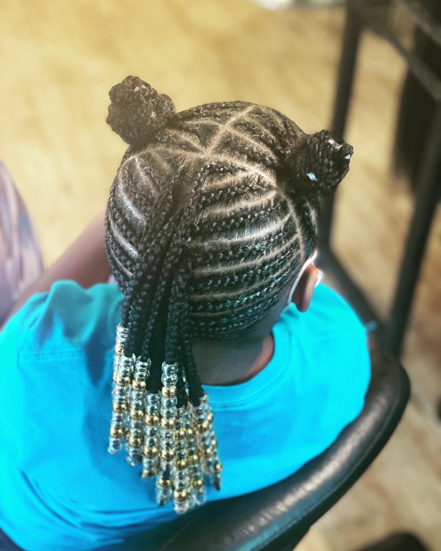 Braided hairstyle with beads and buns, on a person wearing a blue shirt.