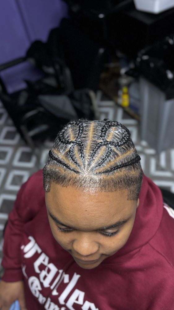 Person with cornrows, wearing a maroon hoodie. Braids are styled in a geometric pattern on top of their head.